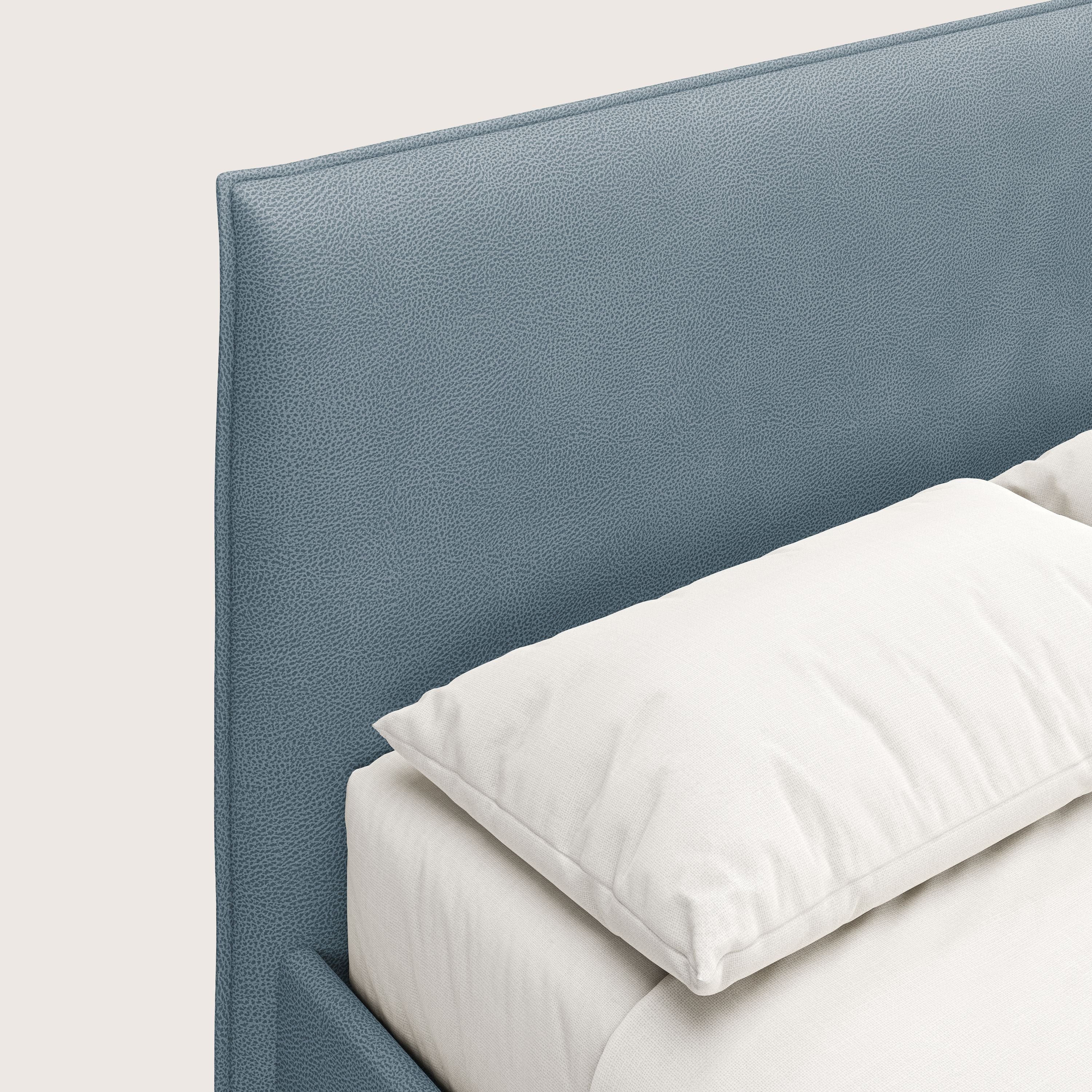 Primo piano di Nina letto contenitore di Letti.store, un letto dal design minimal in smacchiabile carta da zucchero microfibra effetto pelle. La morbida testiera imbottita blu e la biancheria da letto bianca creano un look pulito e contemporaneo.