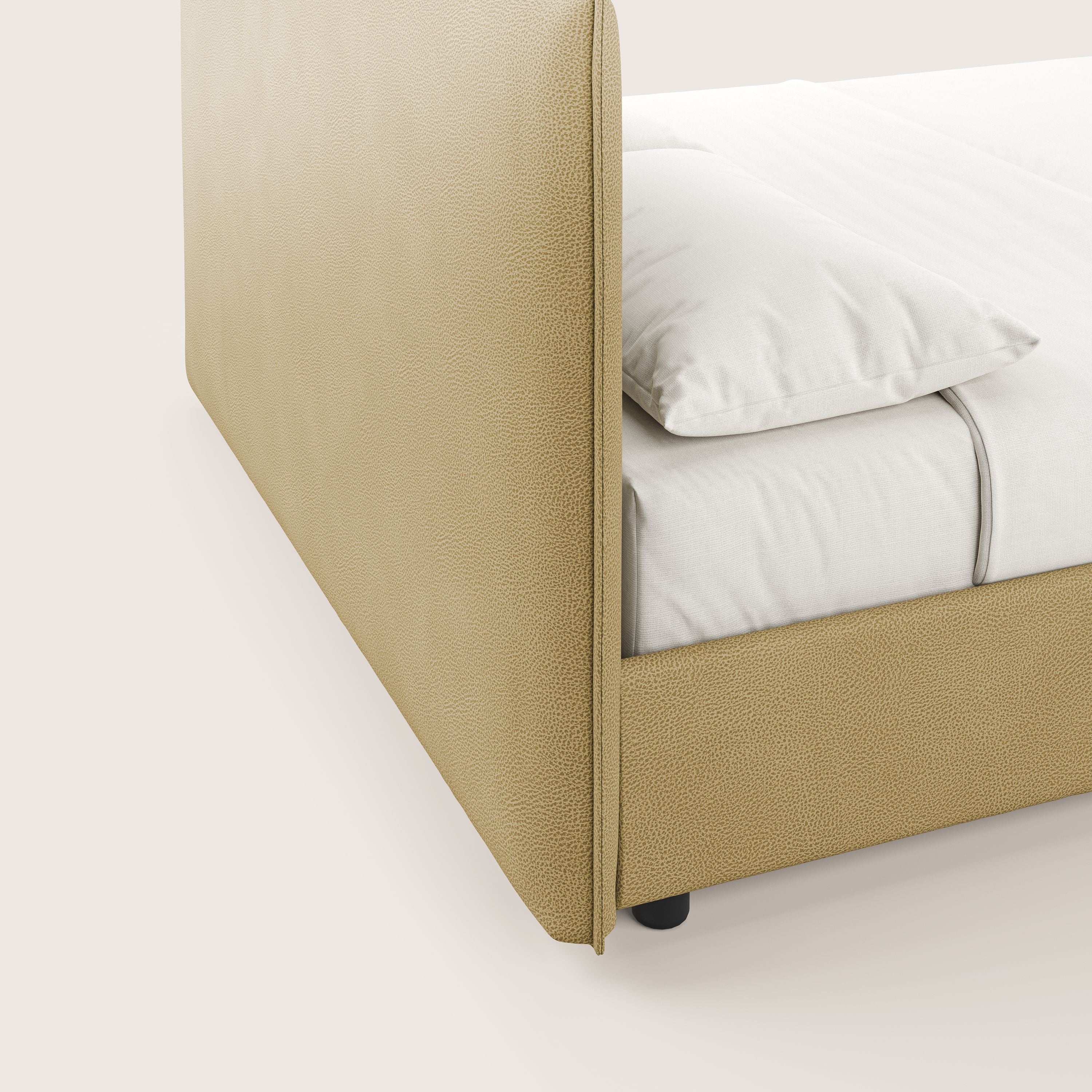 Primo piano del letto contenitore Nina di Letti.store, un letto minimal in microfibra gialla con finitura antimacchia effetto pelle. Presenta biancheria e cuscini bianchi, gambe nere e solo una parte della testata e del materasso sono visibili.