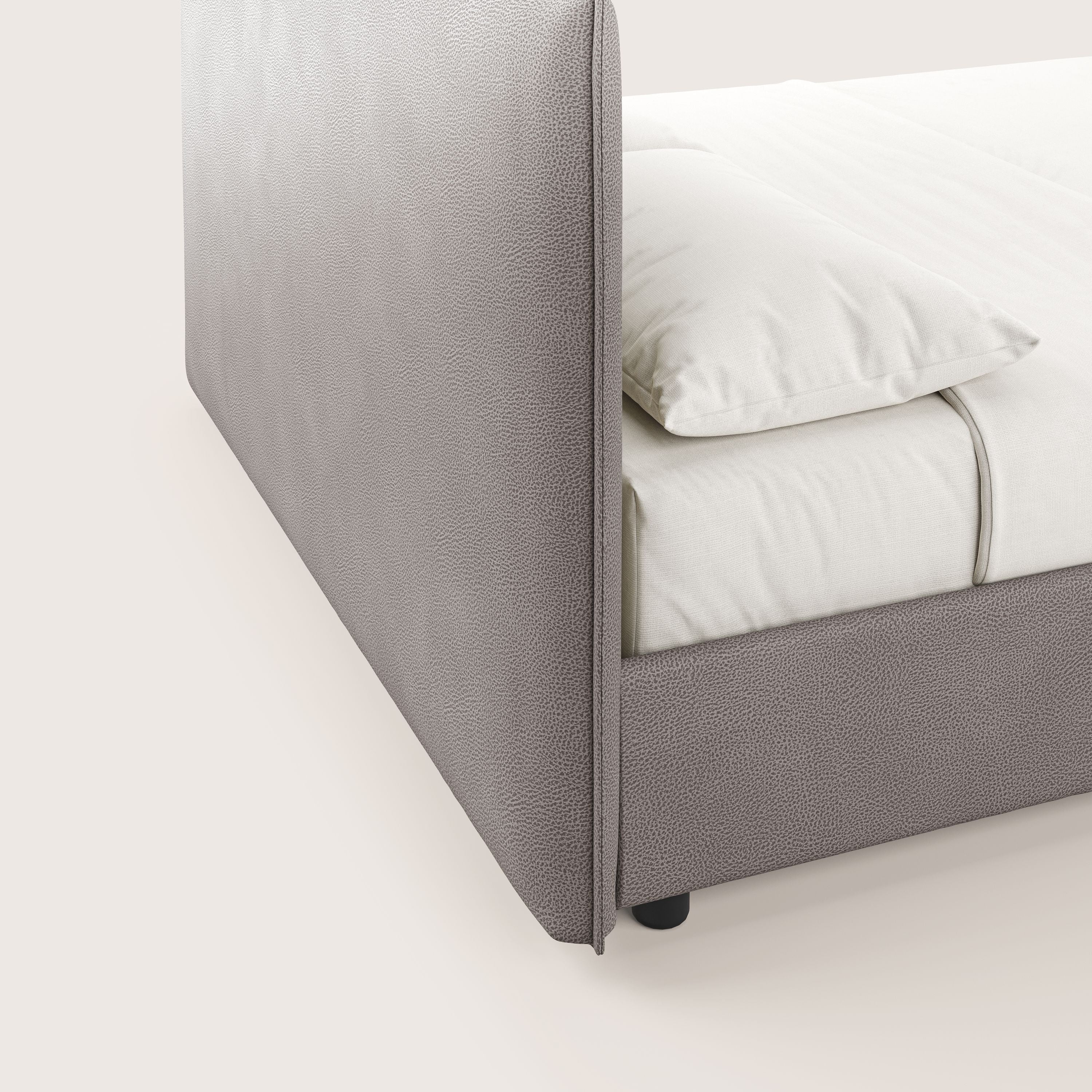 Primo piano del letto contenitore Nina di Letti.store, caratterizzato da un'alta testiera in microfibra tortora testurizzata e da una struttura dal design minimal italiano. La biancheria da letto e i cuscini color crema ne esaltano l'eleganza contro lo sfondo a tinta unita.