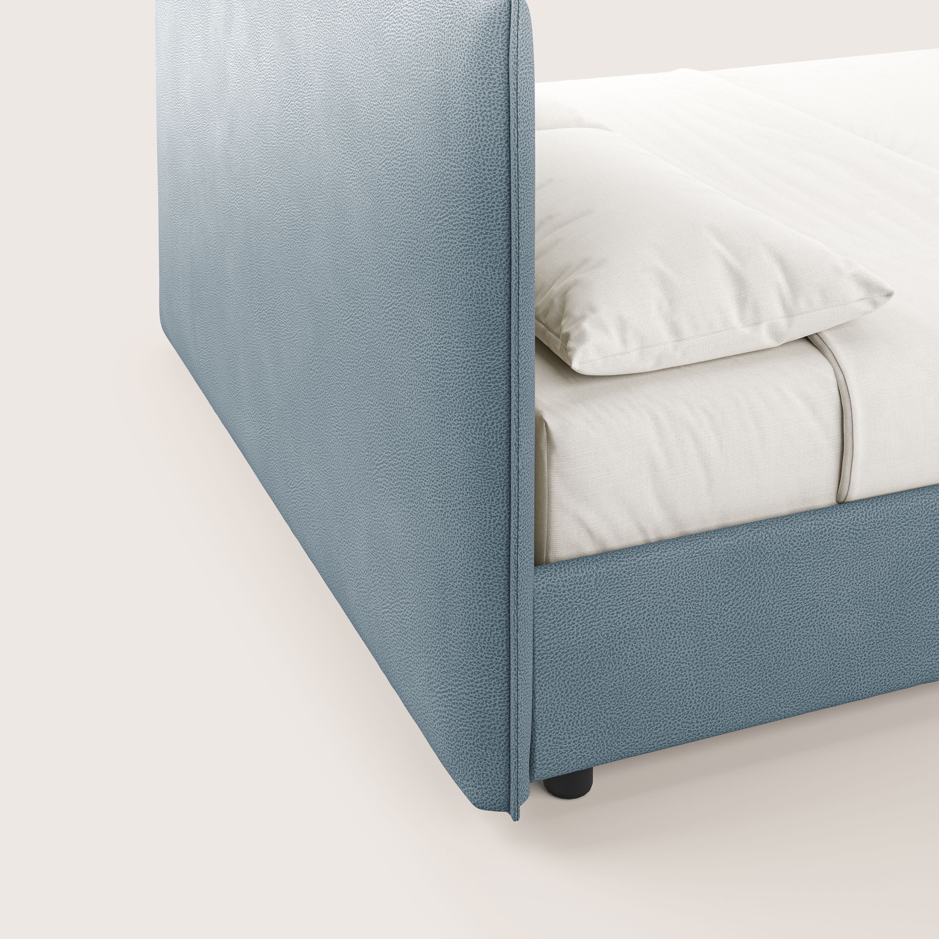 Primo piano del letto contenitore Nina di Letti.store: un letto minimal in smacchiabile carta da zucchero microfibra, con linee pulite e arrotondate, gambe basse nere e biancheria da letto bianca. Lo sfondo è una tonalità neutra e chiara.