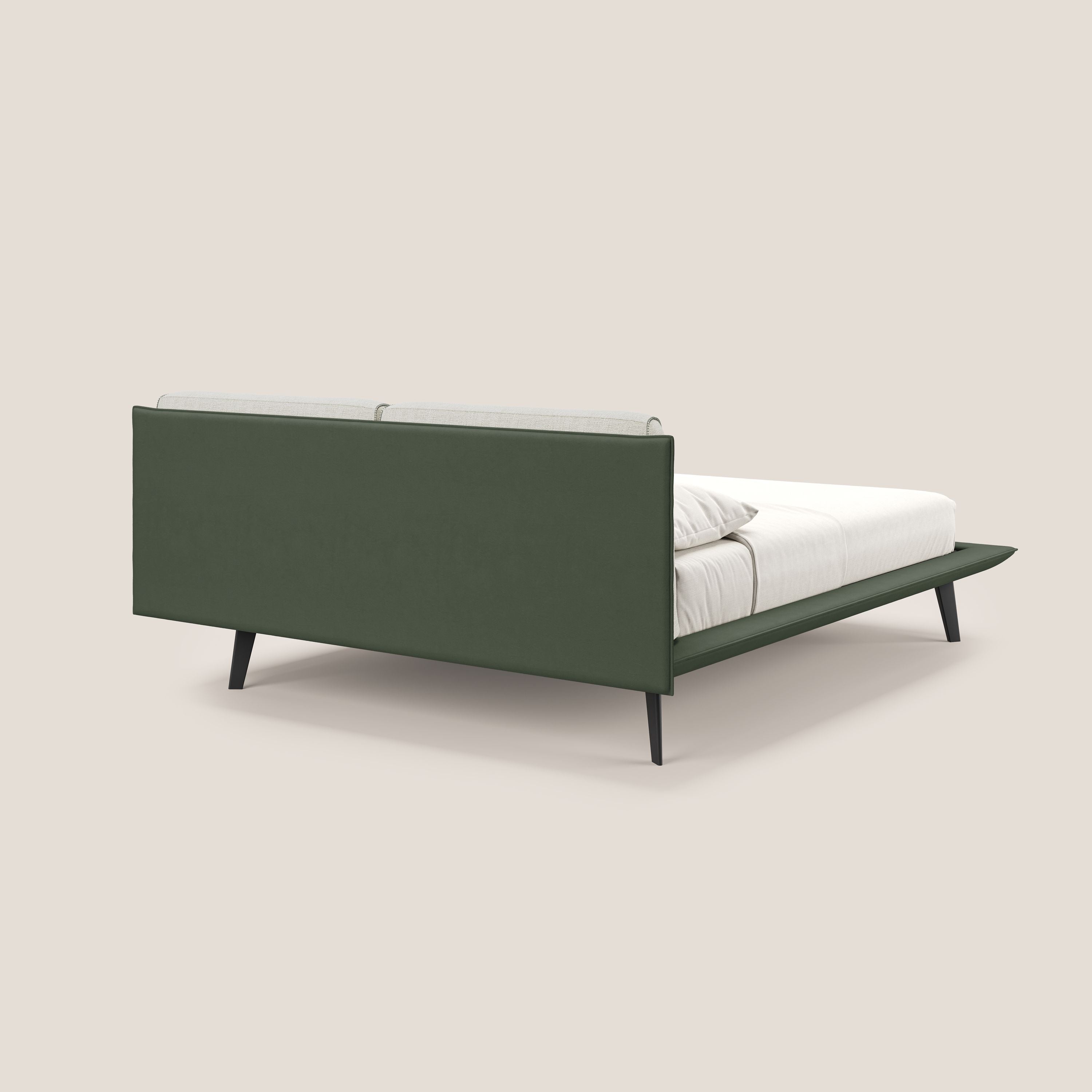 Il letto di design Petra di Letti.store è caratterizzato dal tessuto impermeabile bicolore verde-panna (T11/T06), dai cuscini in piuma e dai piedini angolari in mogano, visto da un angolo posteriore con materasso e cuscini bianchi su sfondo beige.