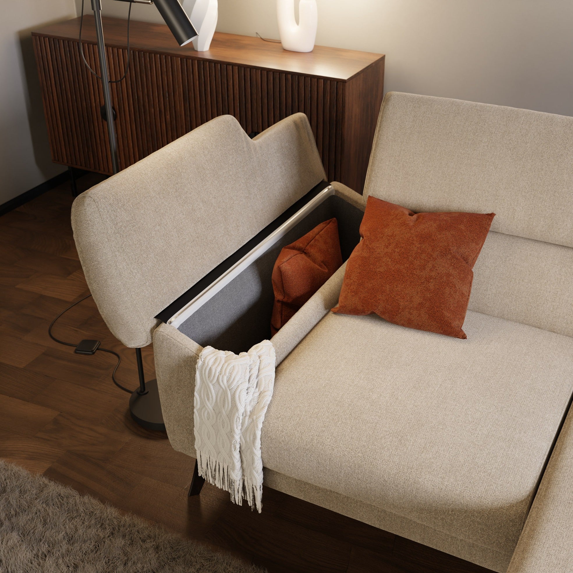 Il Donatello Divano angolare T23 beige di Divani.Store, con braccioli contenitore e poggiatesta, ospita un cuscino ruggine e un plaid bianco. Un altro cuscino è sul sedile; dietro ci sono una credenza in legno, una lampada e una scultura bianca.