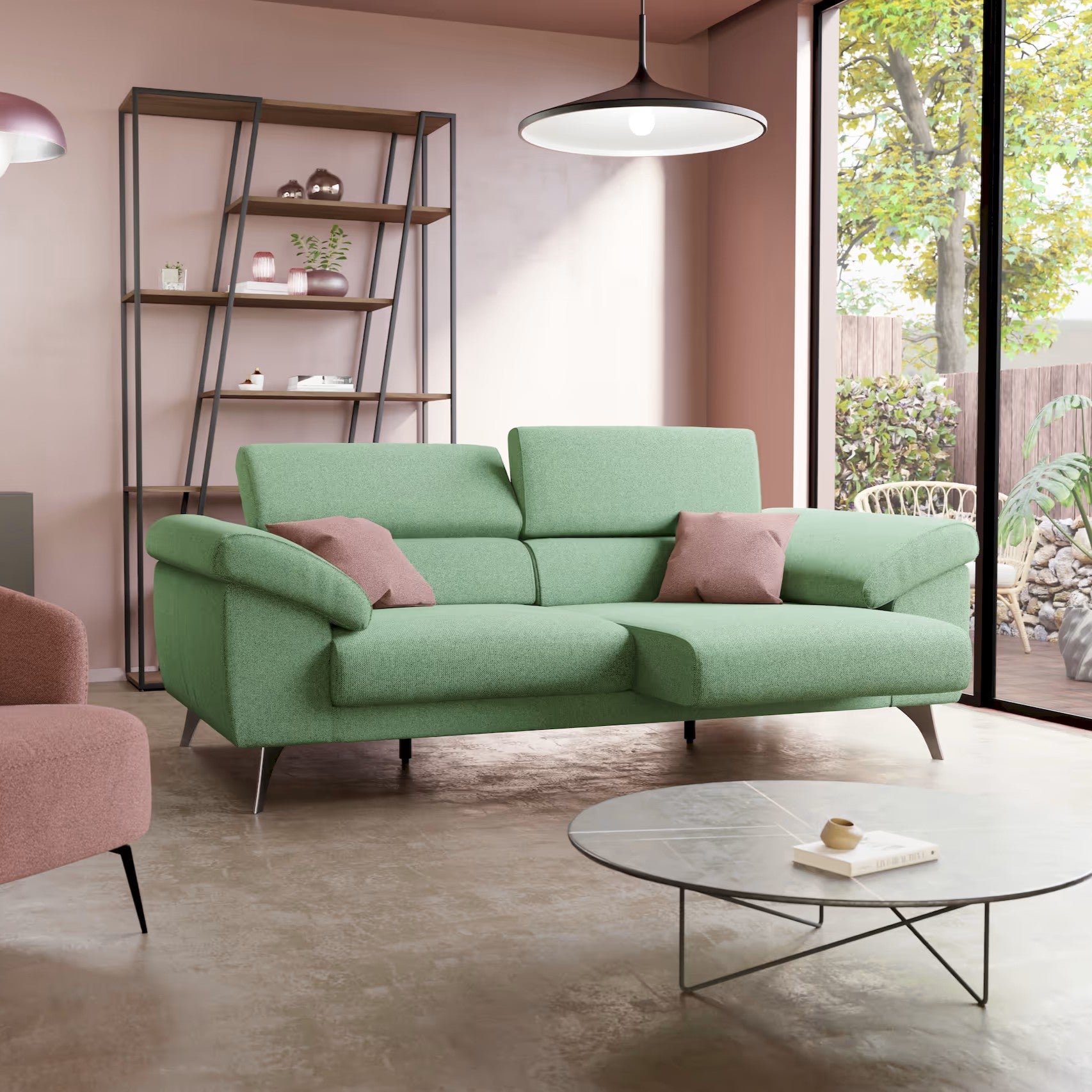 Un soggiorno moderno con il divano Donatello di Divani.Store in T23 menta, con due cuscini rosa, un tavolino rotondo in vetro, una poltrona rosa, una mensola in metallo con decoro, pareti rosa e ampie finestre con vista sugli alberi e sul patio.