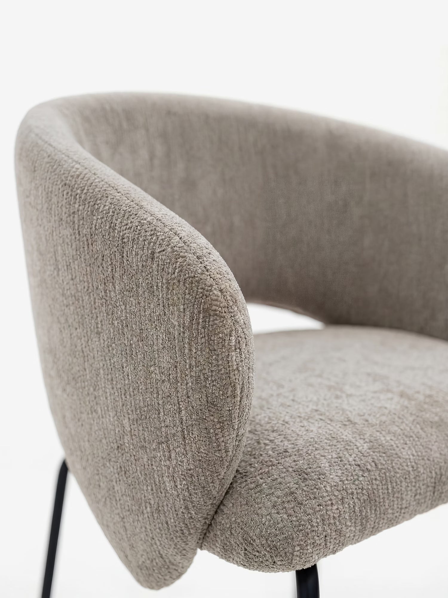 Primo piano della sedia imbottita con braccioli “Fosca” di Divani.Store, caratterizzata da braccioli ricurvi, morbido tessuto beige certificato OEKO-TEX® e sottili gambe in metallo nero. Lo sfondo bianco ne esalta le linee pulite e il design elegante.