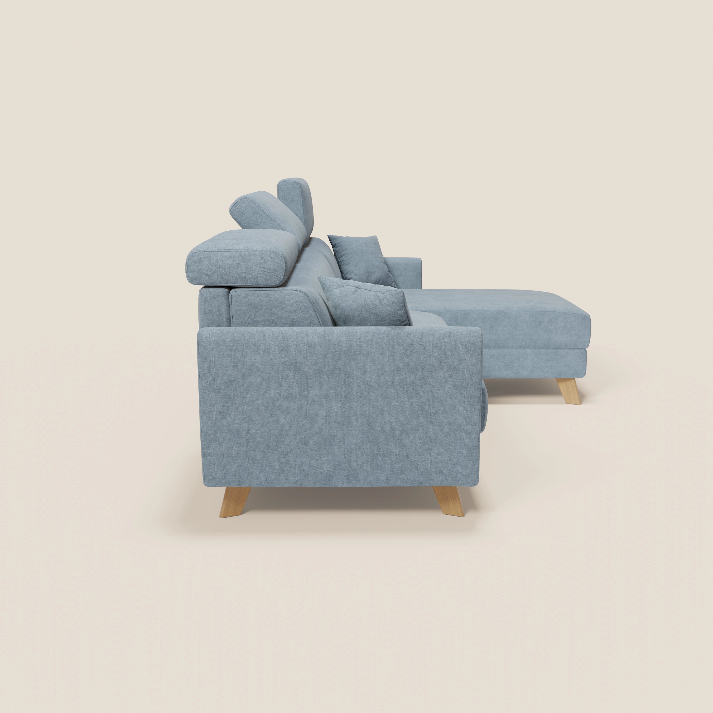 Vista laterale del divano letto angolare Francy di Divani.Store, con rivestimento sfoderabile, chaise longue contenitore e poggiatesta reclinabili in tessuto antimacchia T17 carta da zucchero. Il design elegante si staglia su uno sfondo bianco sporco.