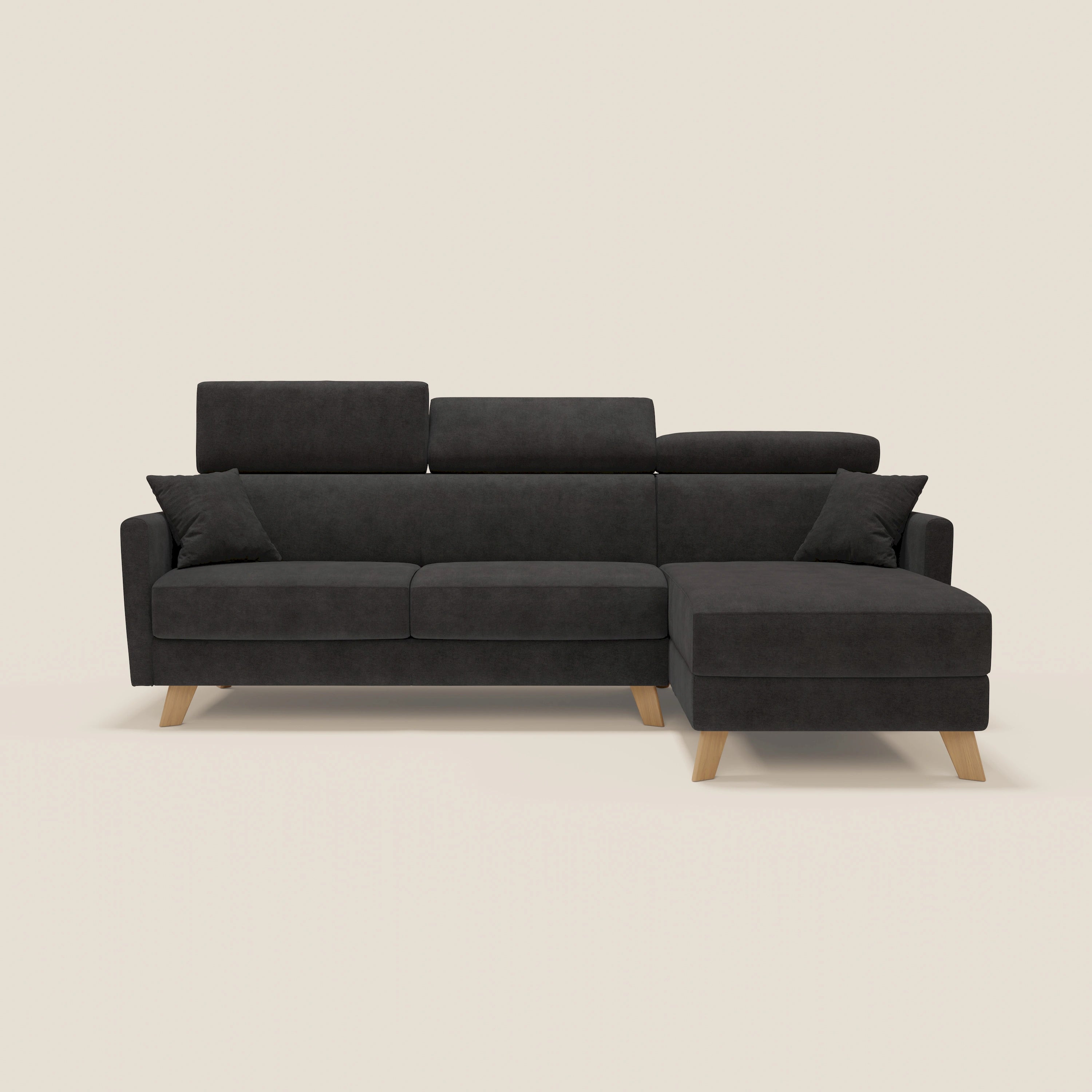 Un moderno divano letto angolare Francy grigio scuro sfoderabile di Divani.Store in T17 nero, con gambe in legno, design in stile nordico, chaise lounge contenitore a destra, poggiatesta reclinabili e due cuscini, su fondo beige tinta unita.
