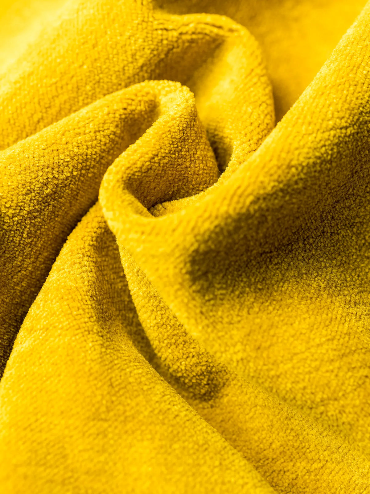 Un primo piano del velluto moderno S05 BRERA, di un vivace giallo senape, morbido al tatto e antimacchia, arricciato in morbide pieghe fluide che creano ombre profonde e riflessi luminosi sulla sua superficie soffice.