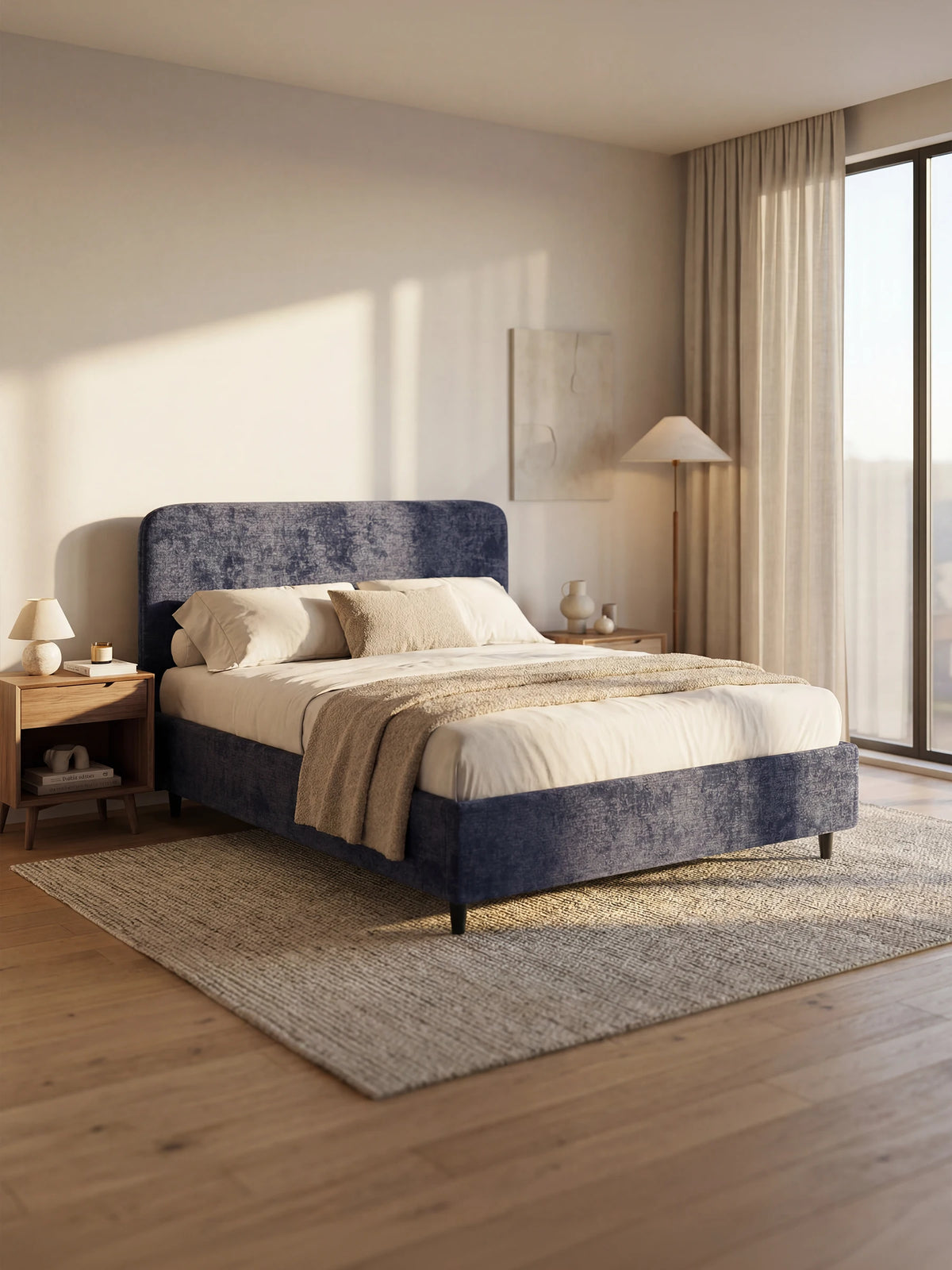 Il letto imbottito KAELOS in stile minimal, caratterizzato da una testiera arrotondata in ciniglia blu scuro, poggia su un tappeto dalla trama ruvida, è rivestito con biancheria da letto dai toni neutri e un copriletto, ed è affiancato da comodini in legno illuminati da una luce morbida e naturale.