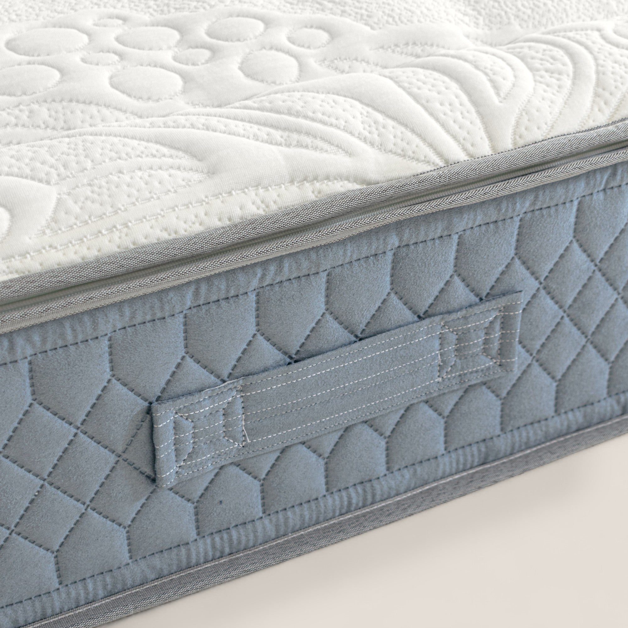 Primo piano di KYROS by Divani.Store: materasso ad angolo con top bianco trapuntato, pannello laterale azzurro, cuciture a diamante, maniglia in tessuto e strati in memory foam per un supporto posturale intelligente a 7 zone.