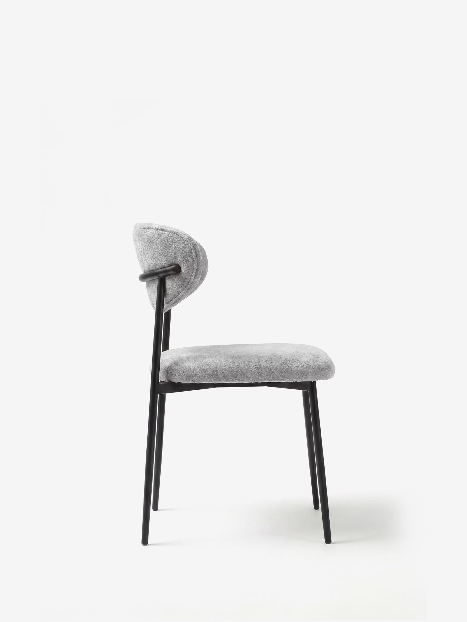 La Luce Sedia, imbottita in morbido tessuto ciniglia, di Divani.Store presenta uno schienale e una seduta curvi e imbottiti in ciniglia grigio chiaro, con sottili gambe in metallo nero e una struttura angolare, raffigurata di profilo su uno sfondo bianco.