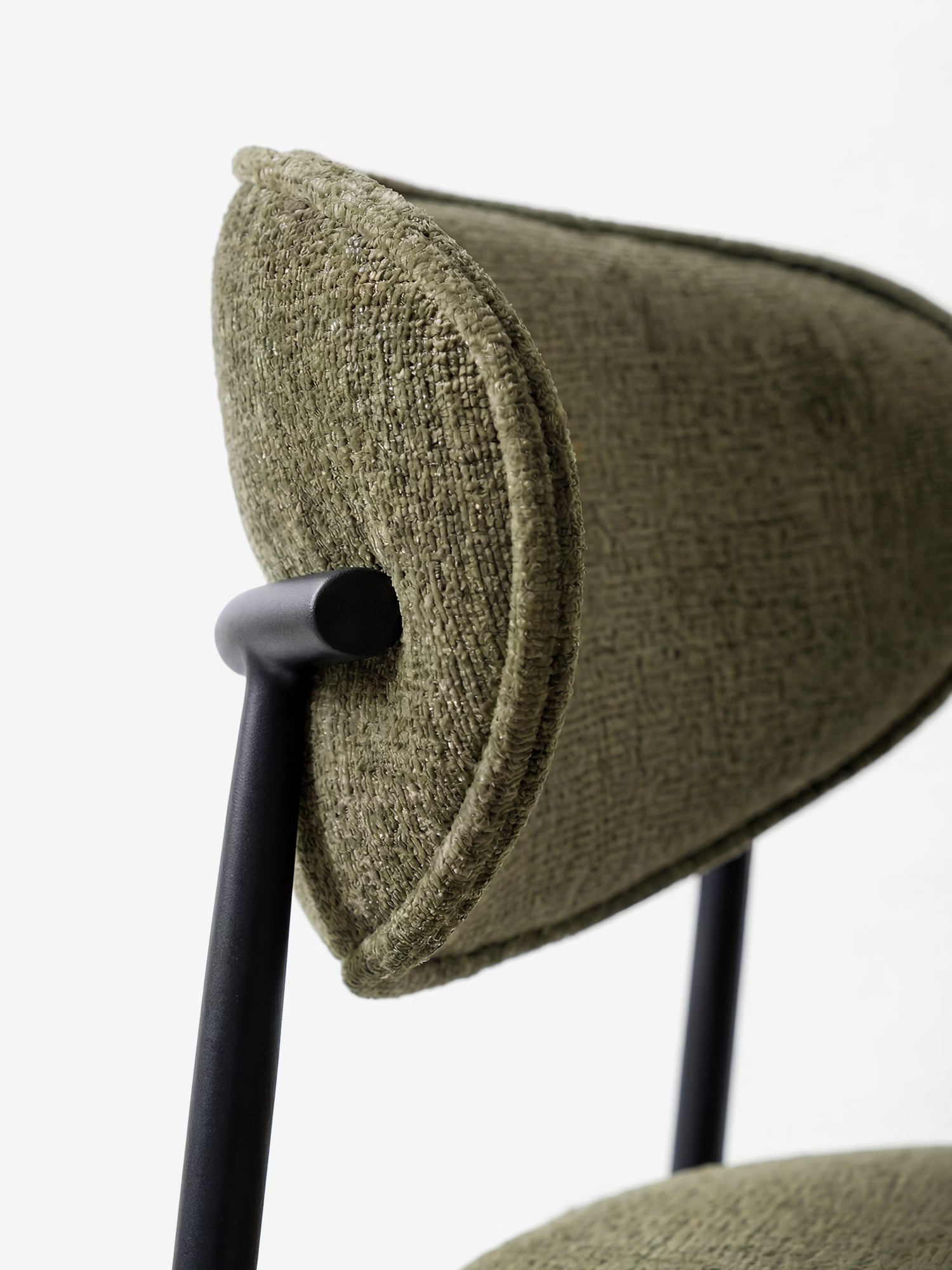 Primo piano della sedia Luce, imbottita in morbido tessuto ciniglia, di Divani.Store, caratterizzata da un rivestimento in ciniglia color verde-oliva e da una struttura in metallo nero opaco. Il design risalta su uno sfondo bianco a tinta unita, conferendo un tocco contemporaneo.