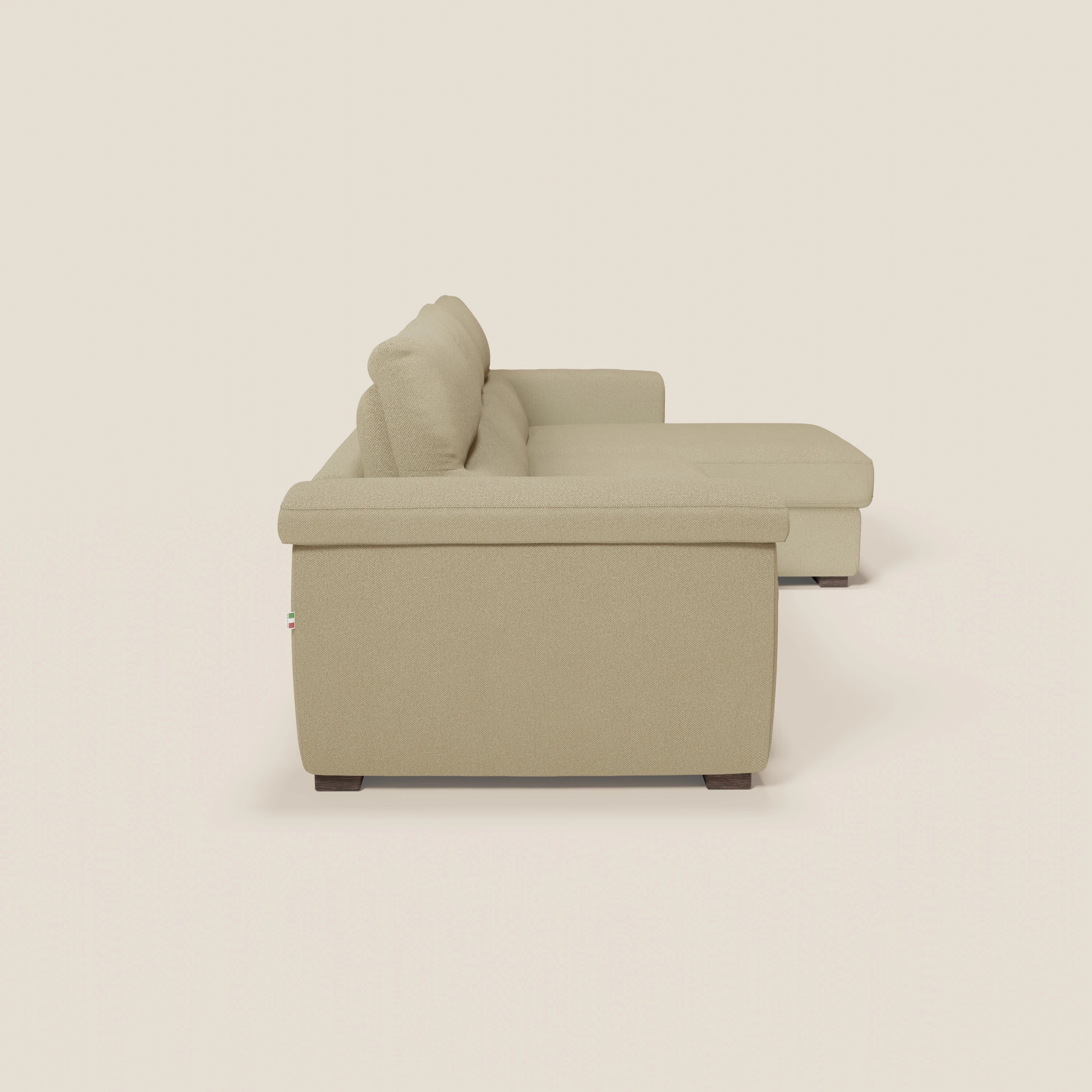 Il divano letto angolare Magnolia con Penisola Contenitore di Divani.Store in tessuto smacchiabile T05 cammello è mostrato in un profilo laterale che mette in risalto i cuscini in tessuto, i piedini in legno e l'imbottitura liscia per il massimo comfort.