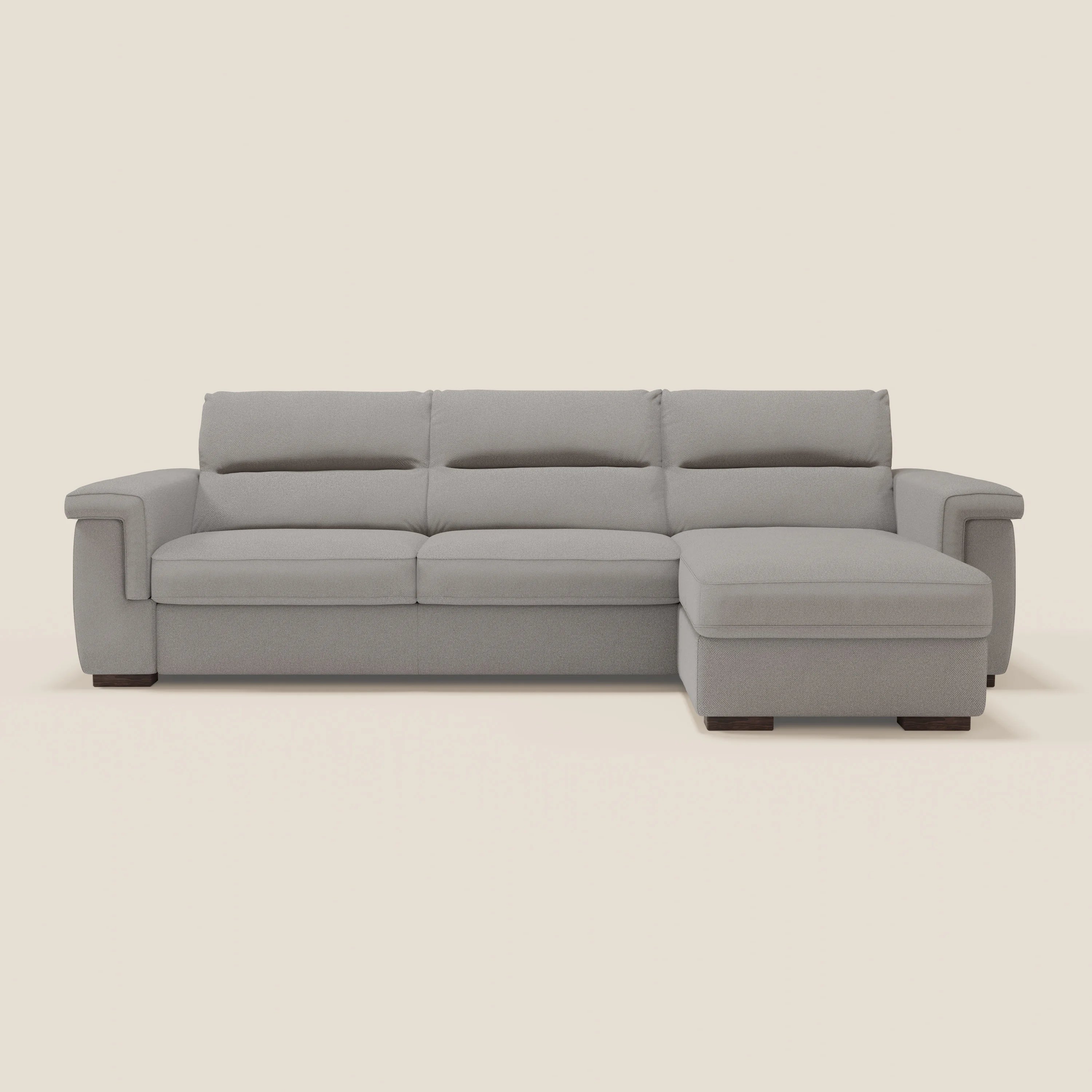Il divano letto angolare Magnolia con Penisola Contenitore di Divani.Store è caratterizzato da un moderno tessuto T05 antimacchia grigio chiaro, tre cuscini di seduta, ampi braccioli, una chaise lounge sul lato destro e gambe in legno scuro a basso profilo.