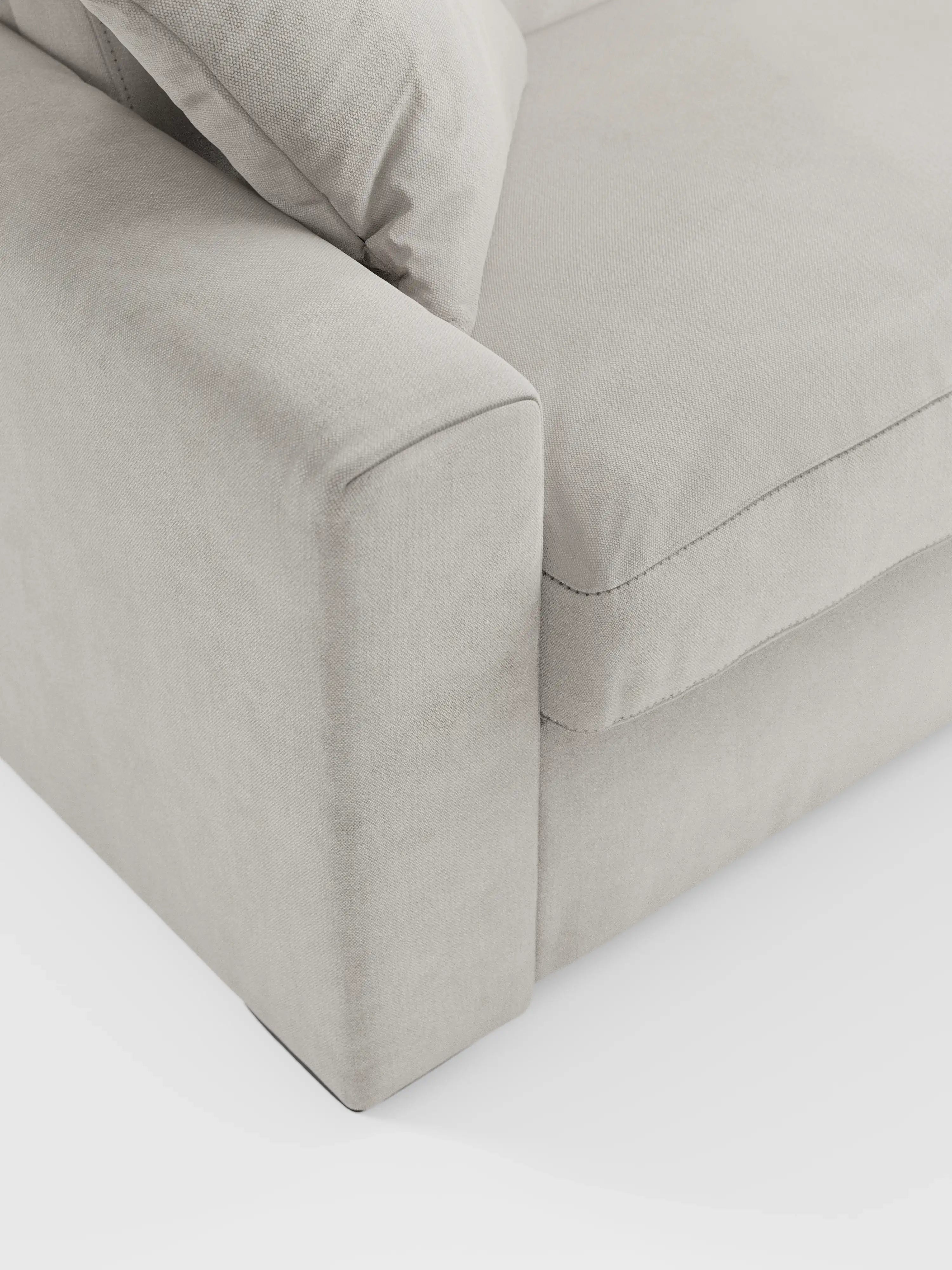 Primo piano del divano letto Maximus a 3 posti con materasso ALTO 20 cm di Divani.Store, presentato in tessuto beige chiaro Oeko-Tex antimacchia. Il divano presenta braccioli ampi e squadrati, seduta imbottita con cuciture a vista e poggiatesta regolabili. L'immagine mette in risalto la morbida trama del rivestimento e le linee pulite su uno sfondo bianco.