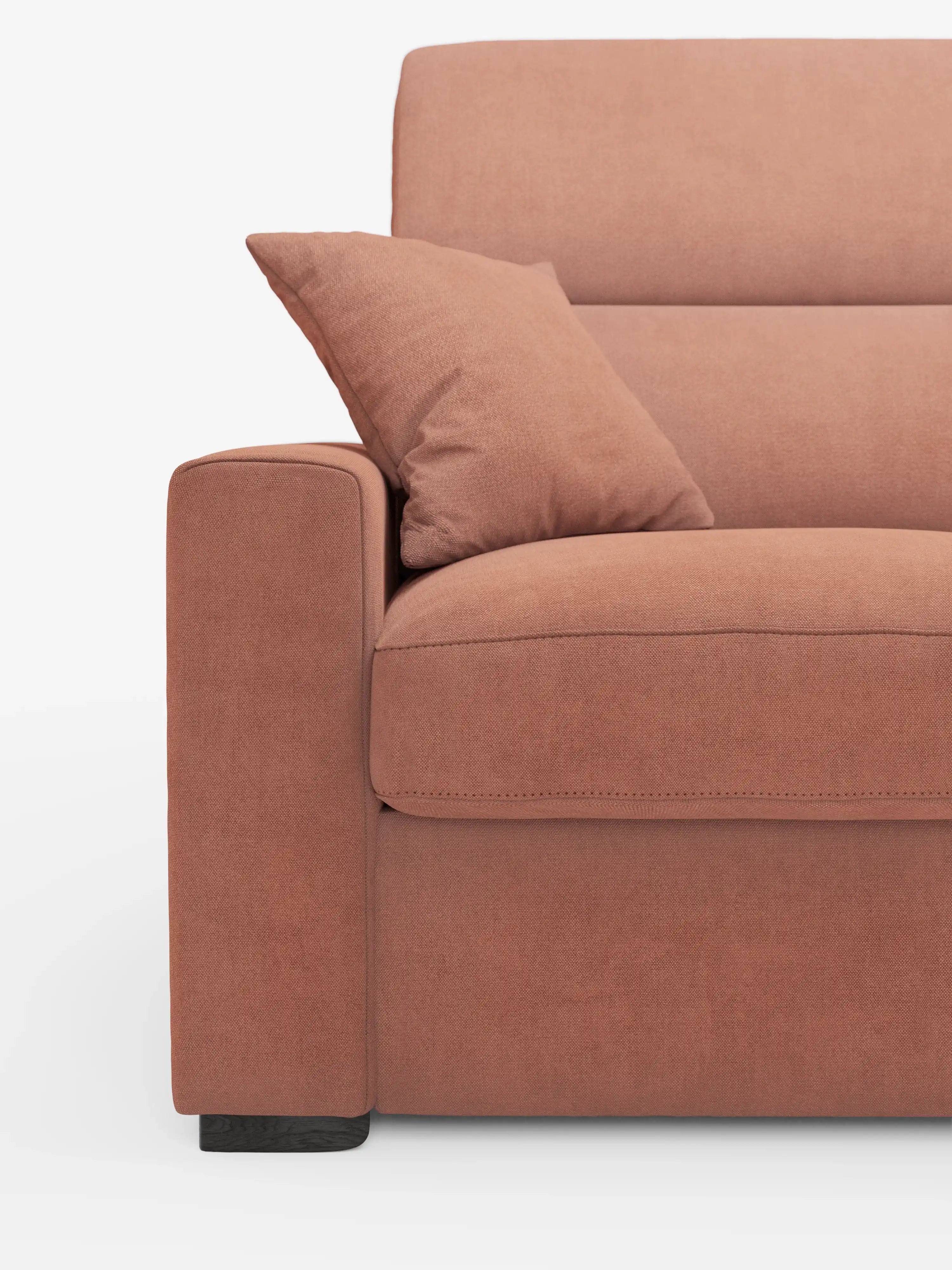 Primo piano del divano letto a 3 posti Maximus di Divani.Store con materasso ALTO da 20 cm, rivestito in tessuto Oeko-Tex color terracotta tenue e resistente alle macchie. L'immagine mette in risalto il bracciolo sinistro, il cuscino della seduta e un cuscino decorativo abbinato. Il divano presenta linee pulite, cuciture a vista, poggiatesta reclinabili regolabili per un maggiore comfort e poggia su gambe corte in legno scuro su uno sfondo bianco.