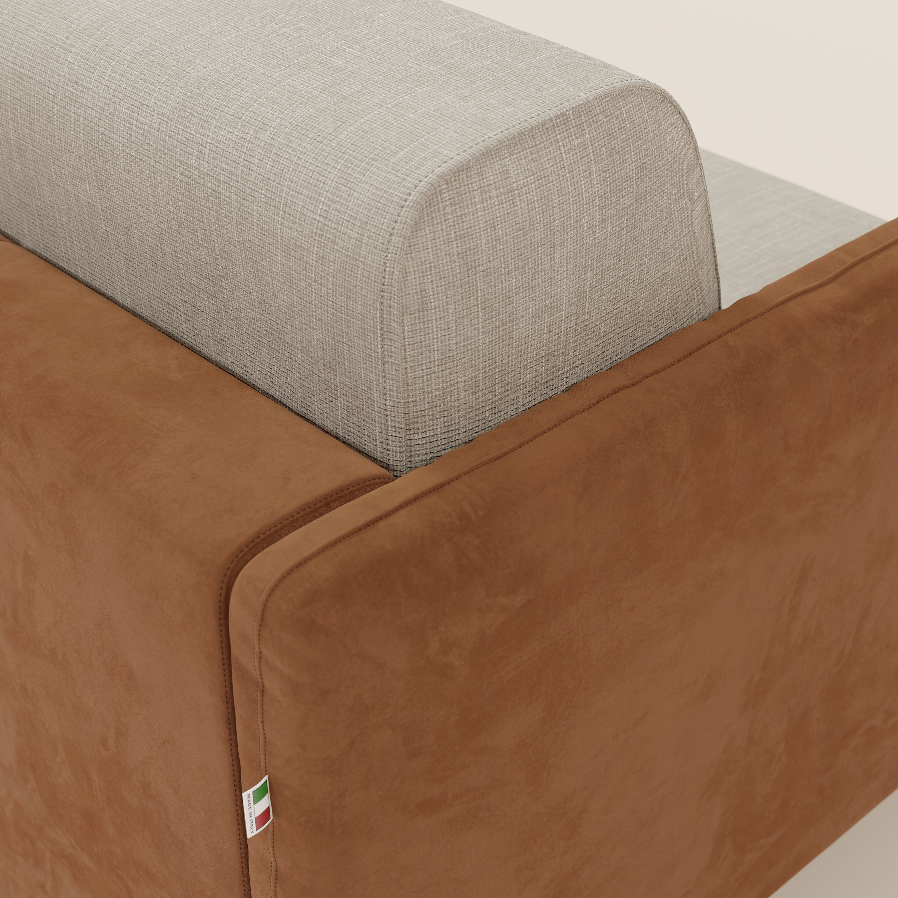 Primo piano del divano letto Narciso di Divani.Store: l'angolo posteriore mostra la struttura in microfibra lavabile color cuoio, lo schienale in tessuto impermeabile color panna e una piccola etichetta con i colori della bandiera italiana. Lo sfondo è una tinta unita chiara.
