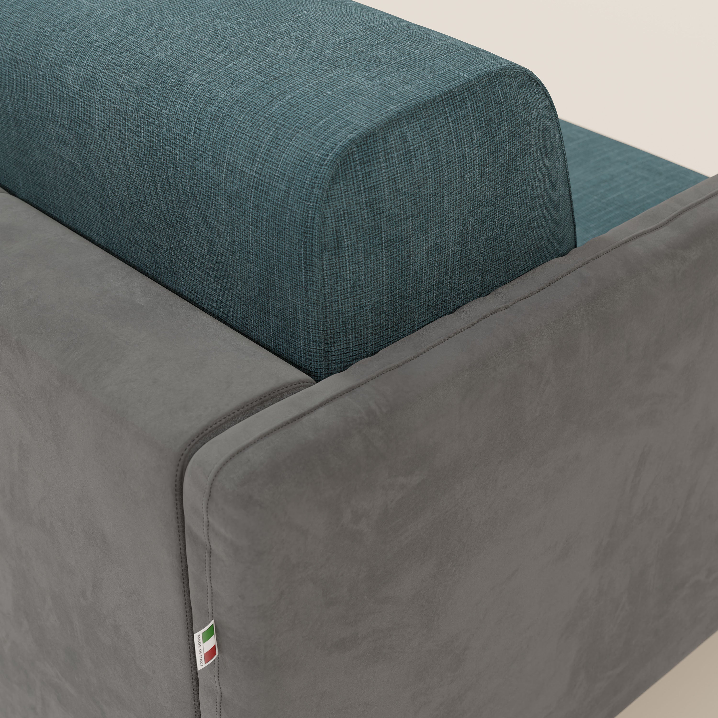 Un primo piano del divano letto Narciso di Divani.Store mostra la microfibra antimacchia nei colori grigio scuro e blu, con schienale testurizzato idrorepellente. Una targhetta con la bandiera italiana sul bracciolo ne sottolinea l'elegante design bicolore e l'artigianalità.