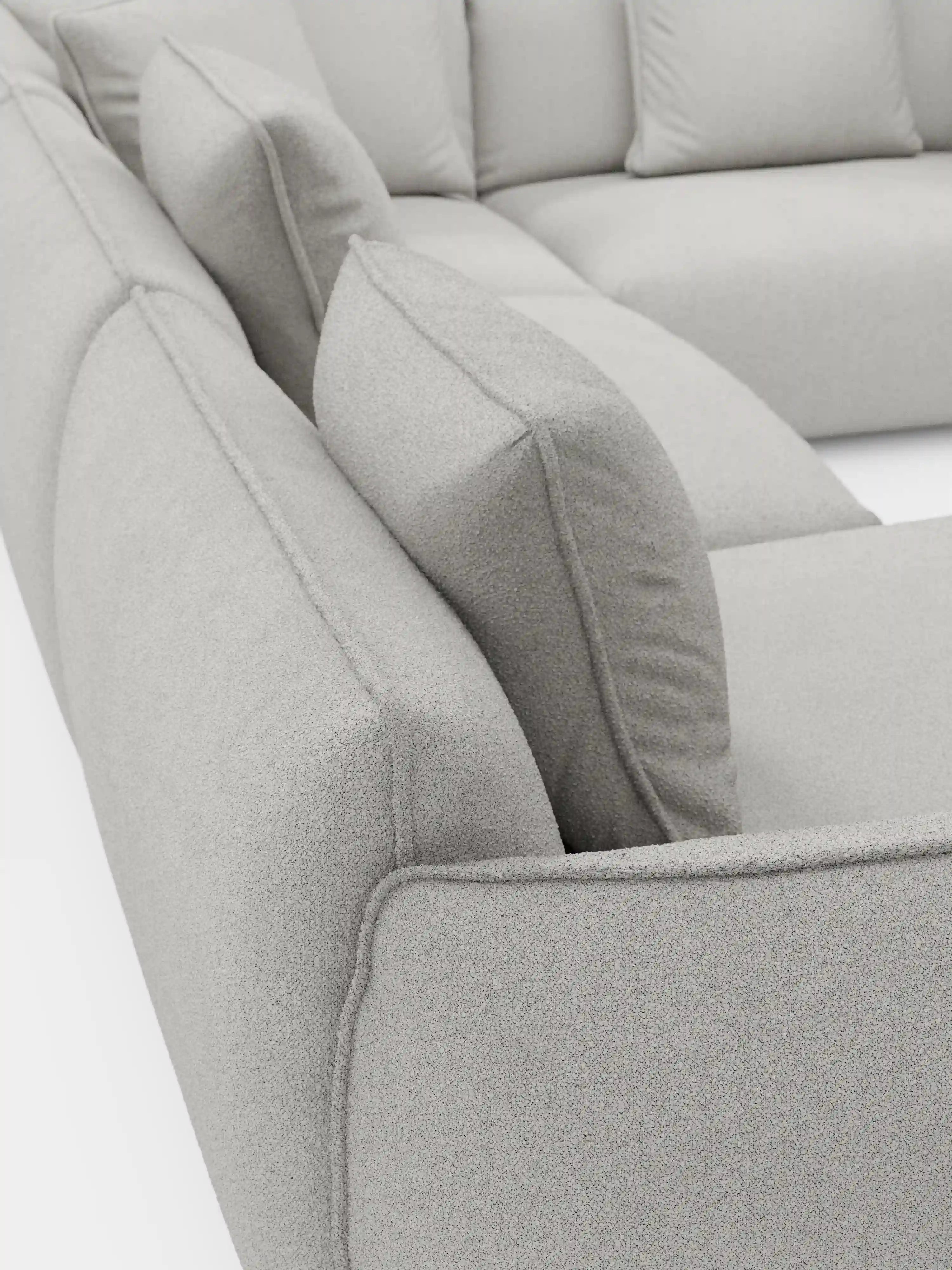 Primo piano del divano angolare panoramico componibile Nimbus con penisola e angolo in tessuto smacchiabile T33 di Divani.Store, caratterizzato da un divano modulare italiano di colore grigio chiaro. I morbidi cuscini quadrati e il tessuto soffice, strutturato e antimacchia mettono in risalto l’imbottitura spessa e le cuciture pulite e moderne. Le sezioni angolari della seduta e dello schienale esaltano sia il comfort che il design contemporaneo.