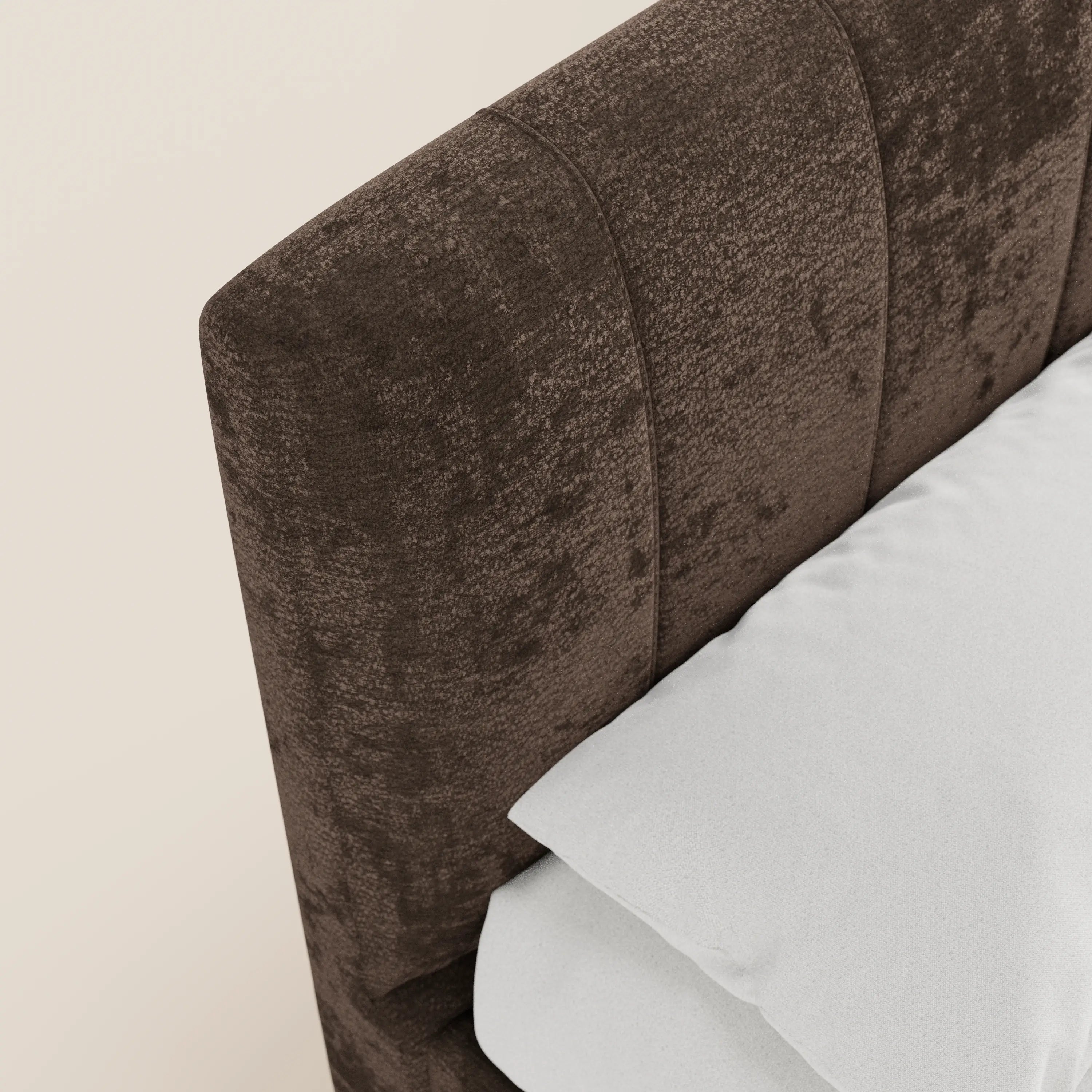 Primo piano del letto imbottito ONYX di Letti.store, caratterizzato da una testiera in tessuto marrone scuro certificato Oeko-Tex® con cuciture verticali. Un cuscino e un lenzuolo bianchi mettono in risalto questo design moderno su uno sfondo beige chiaro.