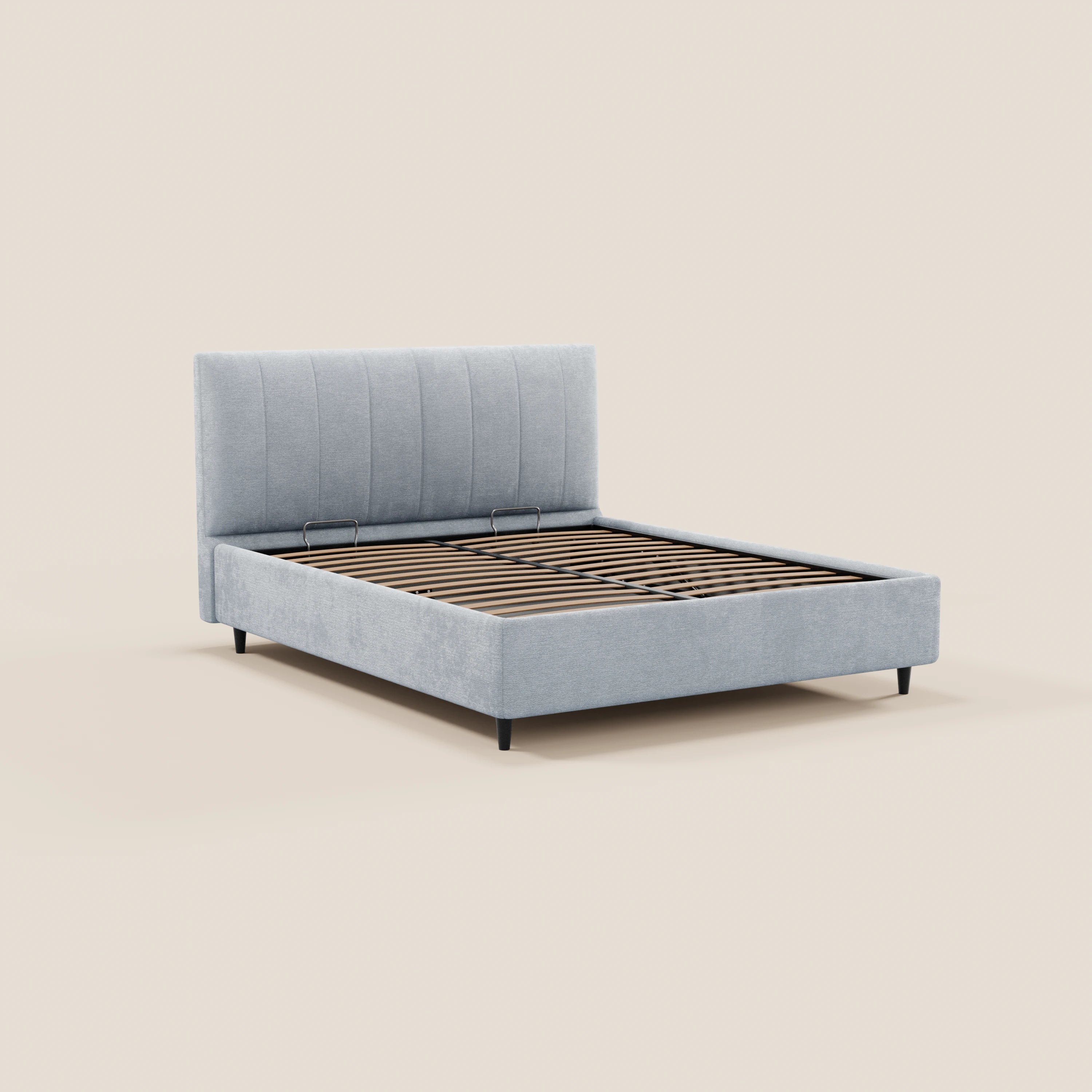 Il letto imbottito con contenitore ONYX di Letti.store presenta una testiera in tessuto grigio chiaro certificato Oeko-Tex® con cuciture verticali, doghe in legno e sottili gambe angolate nere, il tutto su uno sfondo beige a tinta unita.