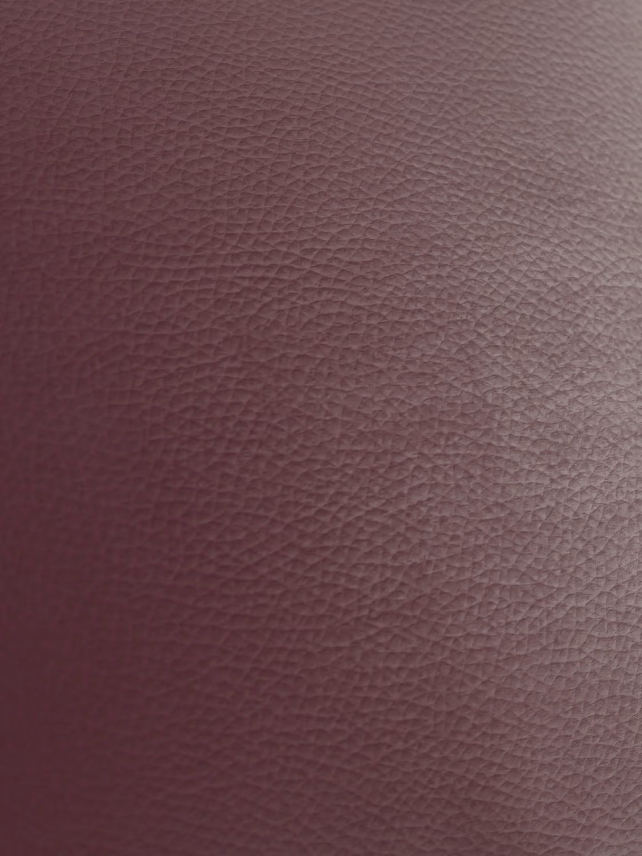 Primo piano della superficie in pelle di colore bruno-rossastro con texture della poltrona Chester, realizzata in vera pelle spessorata con capitonné artigianale da Divani.Store, che rivela sottili venature irregolari su tutto il materiale. L’illuminazione soffusa mette in risalto la texture naturale e le sottili variazioni sia di colore che di finitura superficiale.