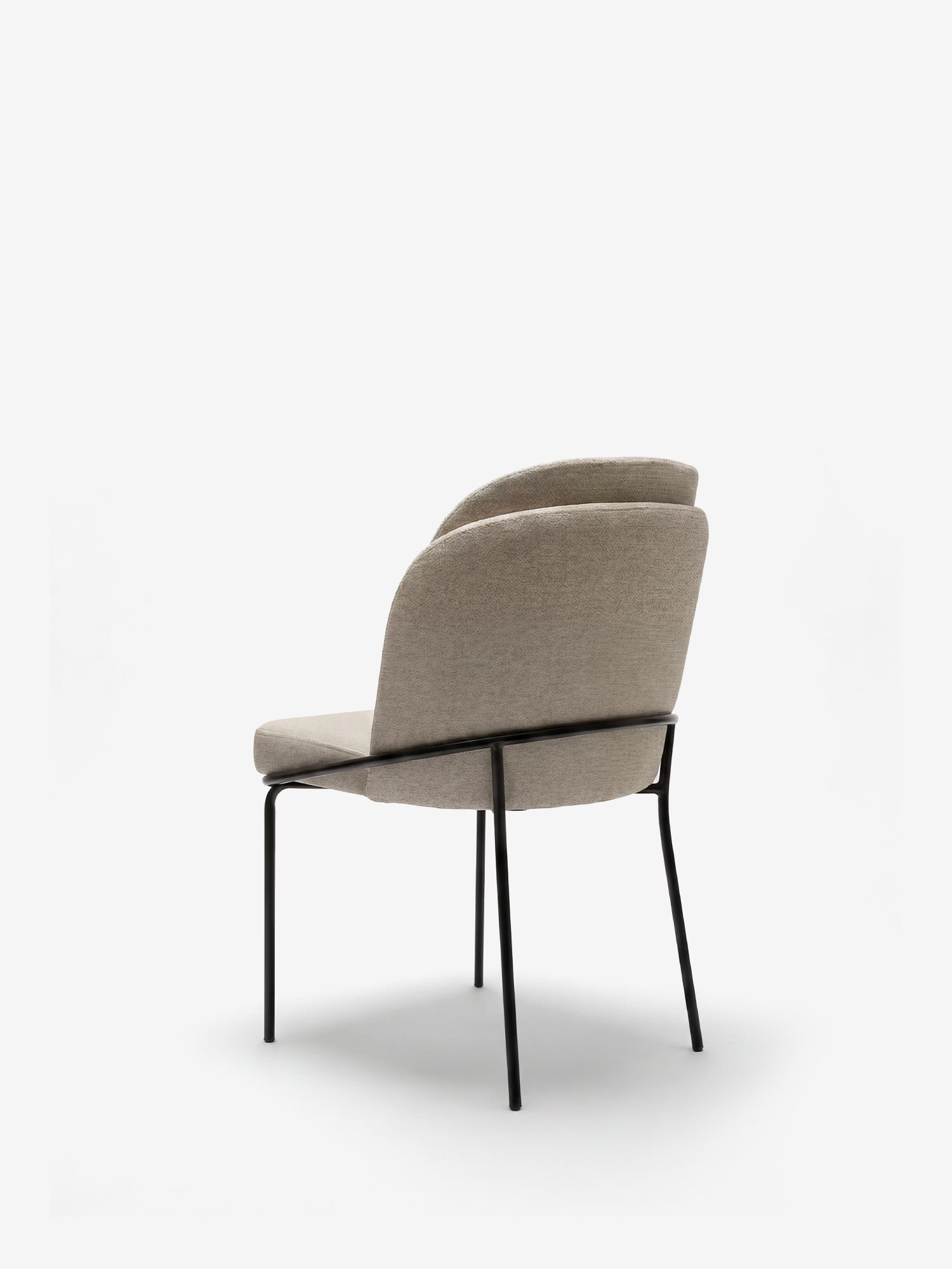 La sedia imbottita Plissè di Divani.Store è caratterizzata da un tessuto impermeabile beige chiaro, uno schienale plissettato e sottili gambe in metallo nero. Ripresa di profilo da dietro su uno sfondo bianco, questa sedia moderna coniuga eleganza e funzionalità.