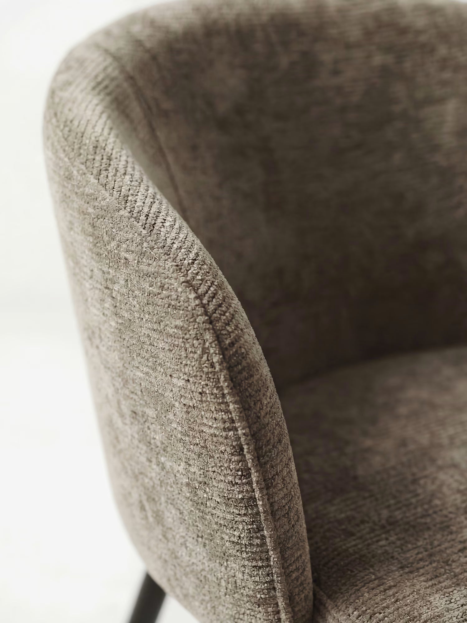 Primo piano della sedia Rovo con braccioli di Divani.Store, caratterizzata da uno schienale ricurvo e da un morbido rivestimento in ciniglia color marrone chiaro. La seduta imbottita e le eleganti gambe in metallo nero ne esaltano il comfort e lo stile contemporaneo. Lo sfondo è leggermente sfocato.