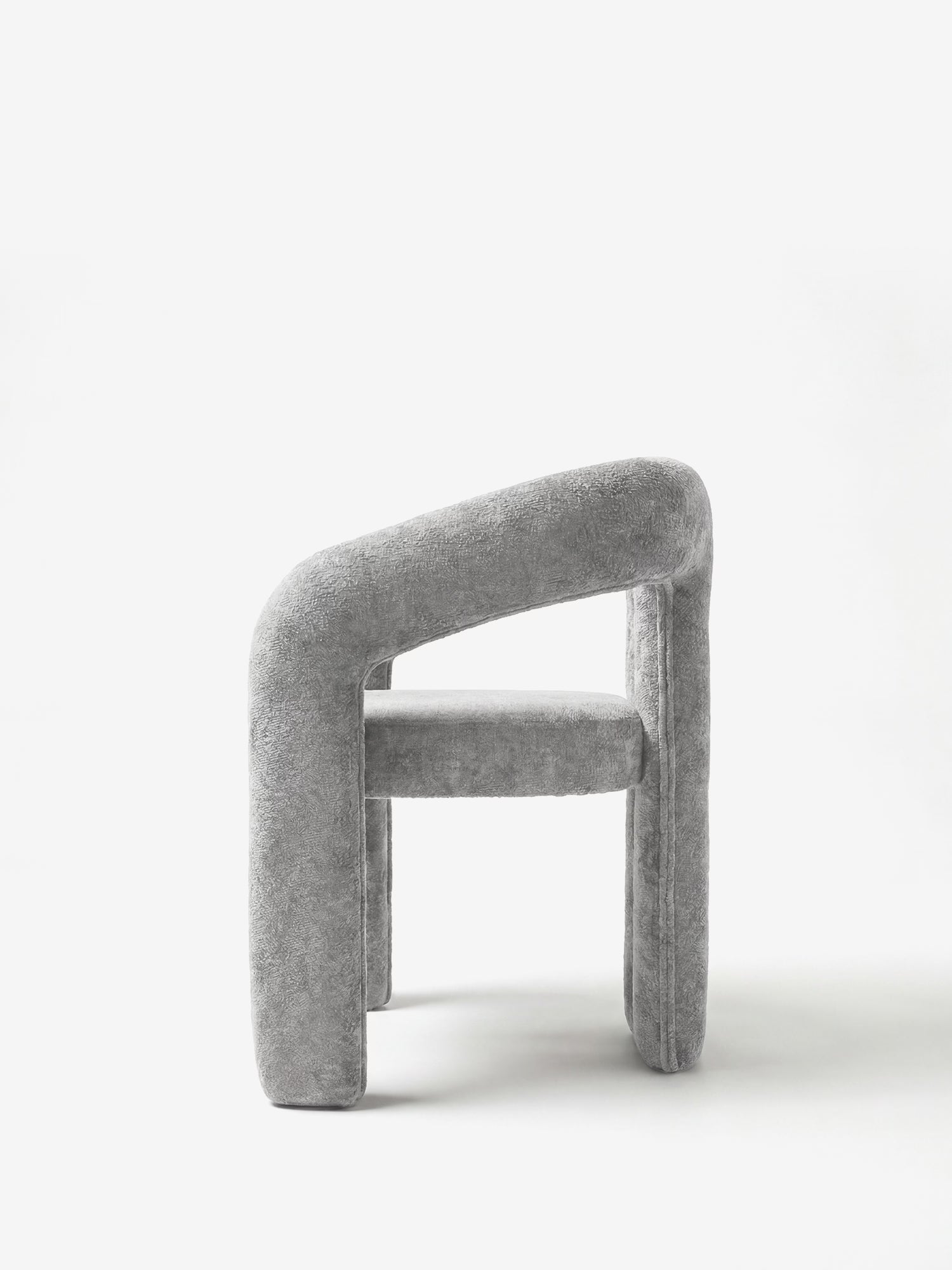 La sedia di design Sibilla di Divani.Store è interamente rivestita in morbido tessuto grigio chiaro; presenta una forma arcuata e gambe e schienale spessi e arrotondati, che le conferiscono un aspetto scultoreo e contemporaneo. Ideale su uno sfondo bianco a tinta unita.