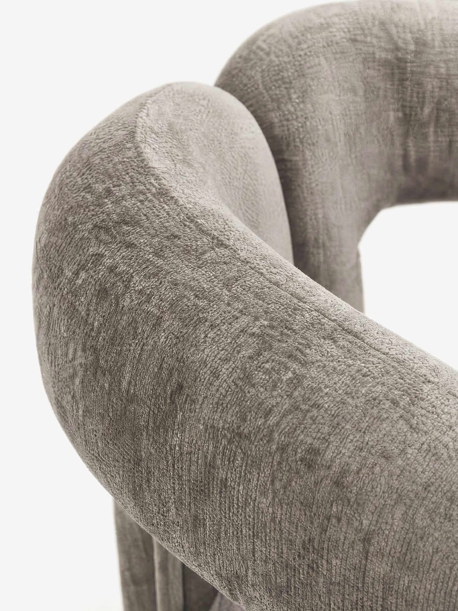 Primo piano della sedia di design Sibilla di Divani.Store, caratterizzata da uno schienale arcuato e da un rivestimento interamente in tessuto di un grigio morbido e materico. La forma circolare avvolgente e l'elegante texture risaltano sullo sfondo bianco.