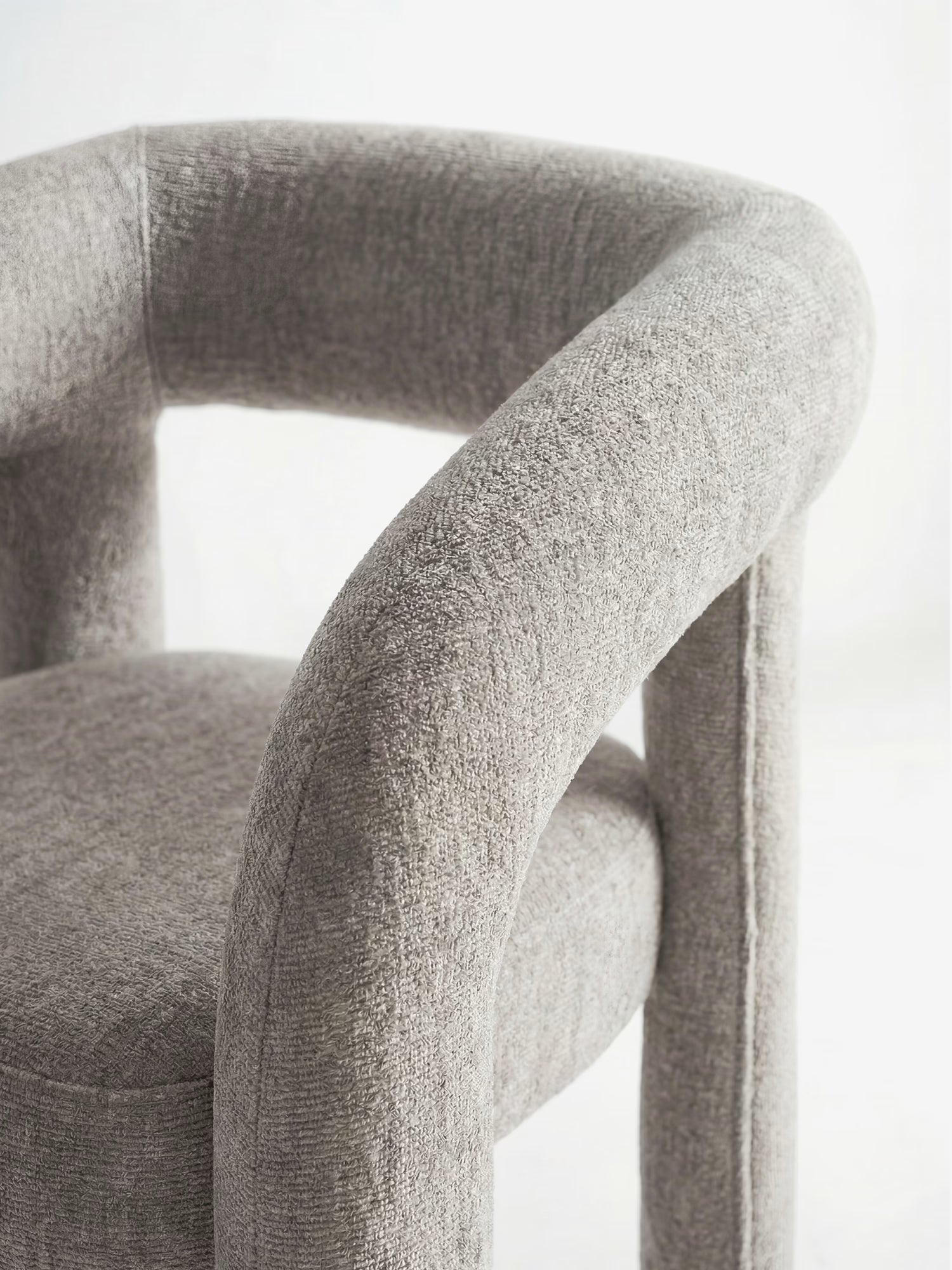 Un primo piano della Sibilla, sedia di design imbottita di Divani.Store, caratterizzata da una struttura ad arco interamente imbottita con spesse imbottiture cilindriche e un morbido tessuto grigio chiaro dalla trama rigata, raffigurata su uno sfondo bianco a tinta unita.