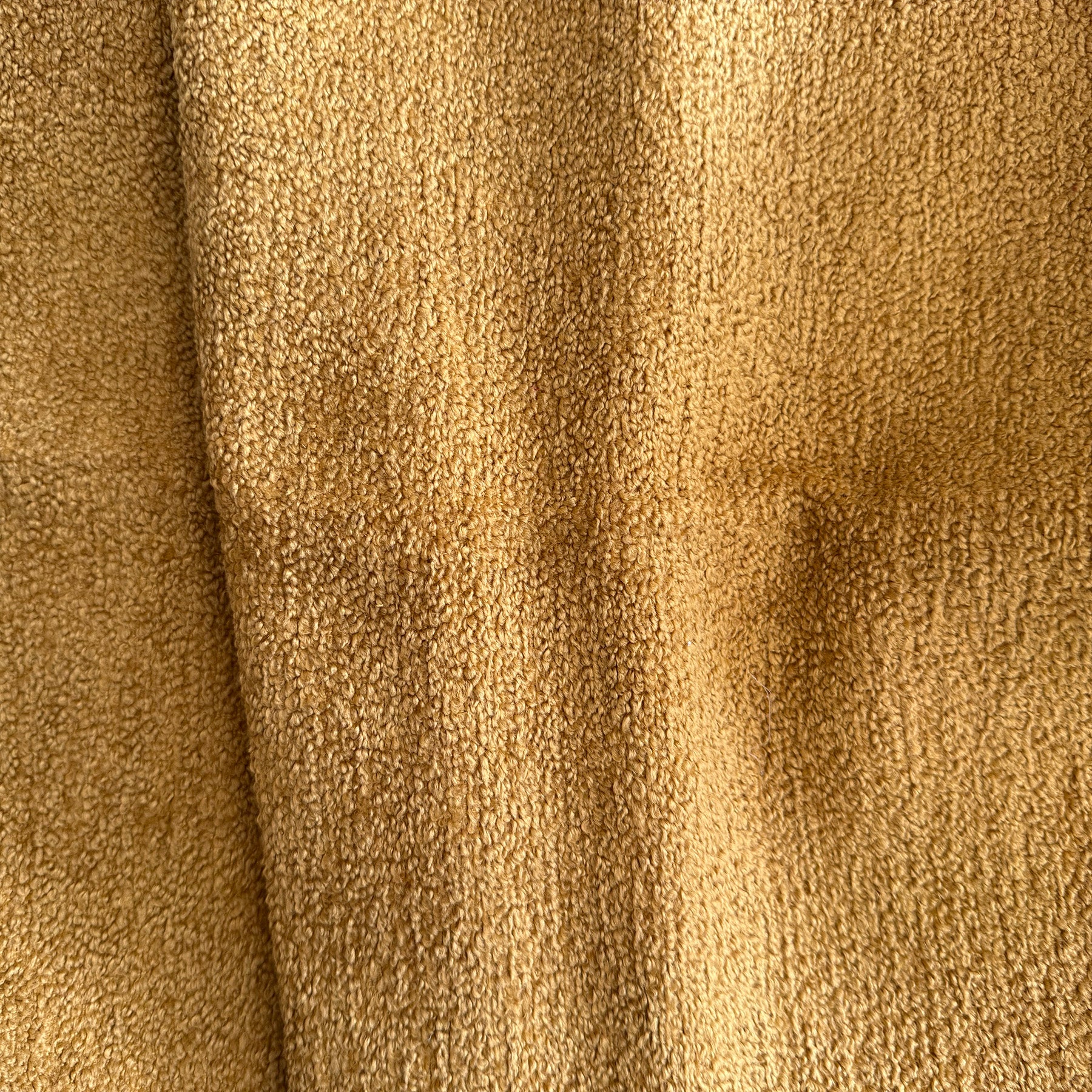 Primo piano di T21 Favola di Divani.Store, un tessuto bouclé morbido ed elegante in un caldo marrone dorato dall'aspetto vellutato e strutturato. Presenta piccole fibre dense, pieghe visibili e ombre. Trattato per essere impermeabile e smacchiabile.