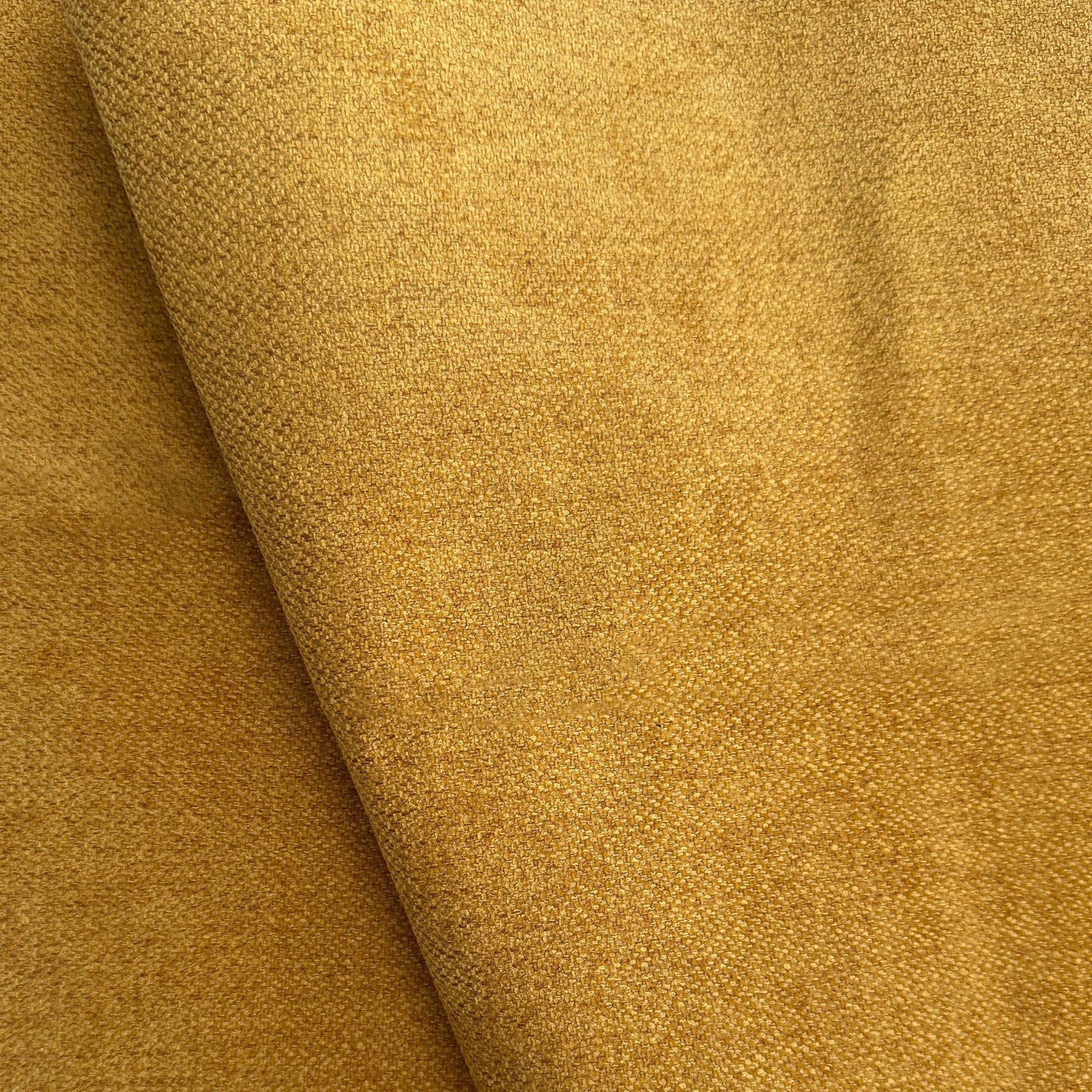 Un primo piano di T23 Strike di Divani.Store mostra la sua morbida texture scamosciata marrone dorato e la sua finitura opaca. Questo tessuto per divani è smacchiabile, irrestringibile, pet-friendly e presenta una grana fine con toni caldi e terrosi.