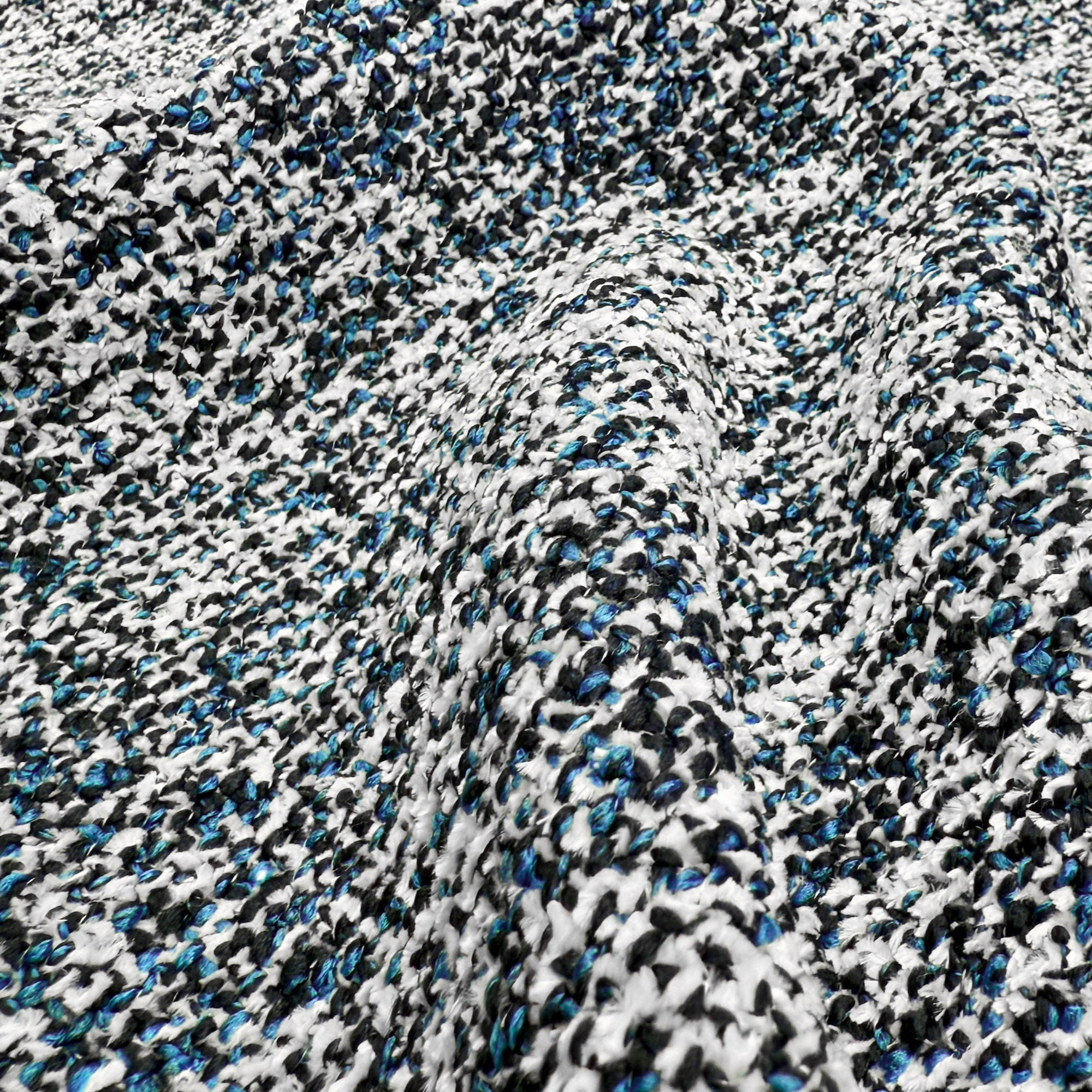 Primo piano di T29 Magnolia pregiato tessuto Bouclé Mélange di Divani.Store: un tessuto morbido e strutturato con fili neri, bianchi, blu e grigi in un bouclé maculato, simile al tweed, con pieghe delicate e un intreccio 3D di tendenza.