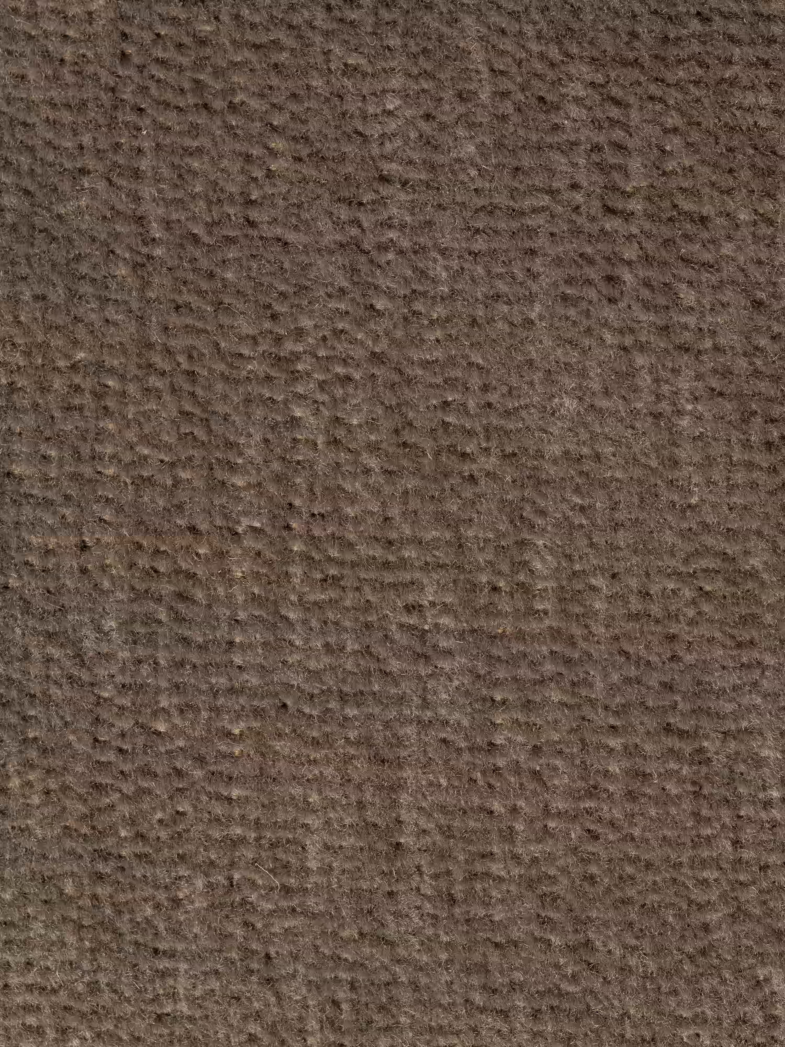 Primo piano di una superficie marrone ruvida che ricorda un tessuto grezzo o della carta consumata, con piccole creste irregolari e sottili linee orizzontali e verticali che formano un motivo naturale, leggermente a griglia. Le delicate variazioni cromatiche le conferiscono un aspetto vissuto, che ricorda l’accogliente rivestimento smacchiabile T31 presente sulla linea Basalto Divano lineare a 2 o 3 posti bicolore con seduta unica e base in metallo di Divani.Store.