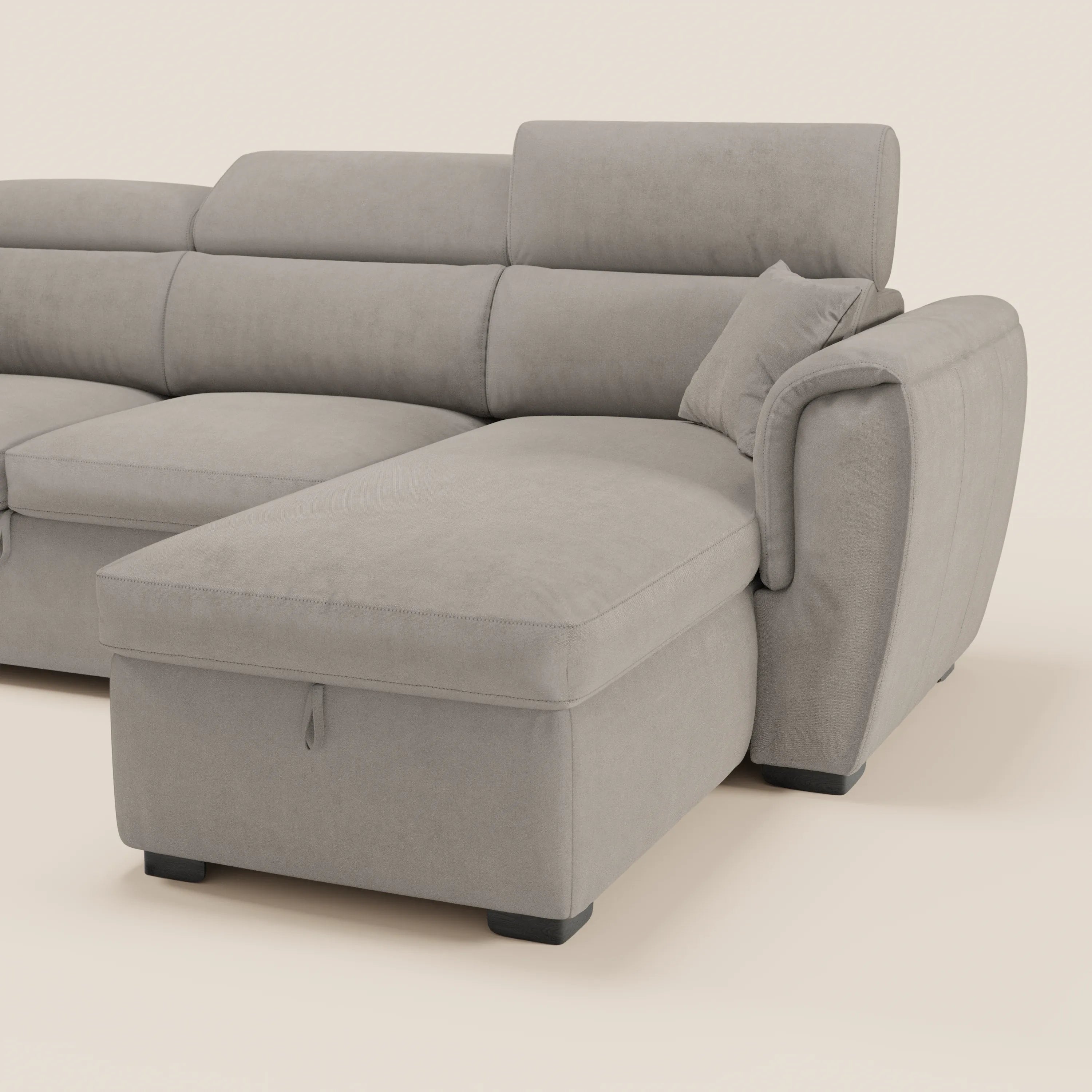 Il divano letto Titano con penisola reversibile di Divani.Store, in tessuto smacchiabile grigio chiaro, è dotato di poggiatesta reclinabili, elemento estraibile e vano contenitore, morbidi cuscini e piedini neri squadrati su sfondo beige.