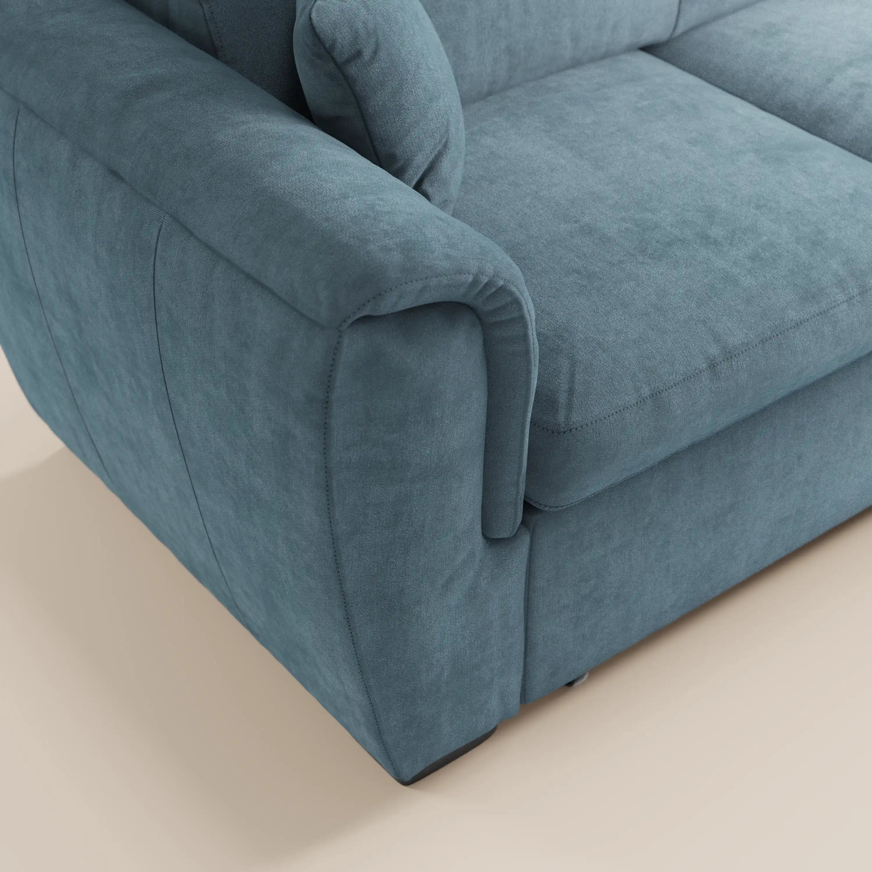 Primo piano del divano letto Titano con penisola reversibile di Divani.Store, rivestito in tessuto blu-grigio antimacchia con poggiatesta reclinabili, elemento estraibile e cuciture di pregio su una superficie morbida e vellutata.