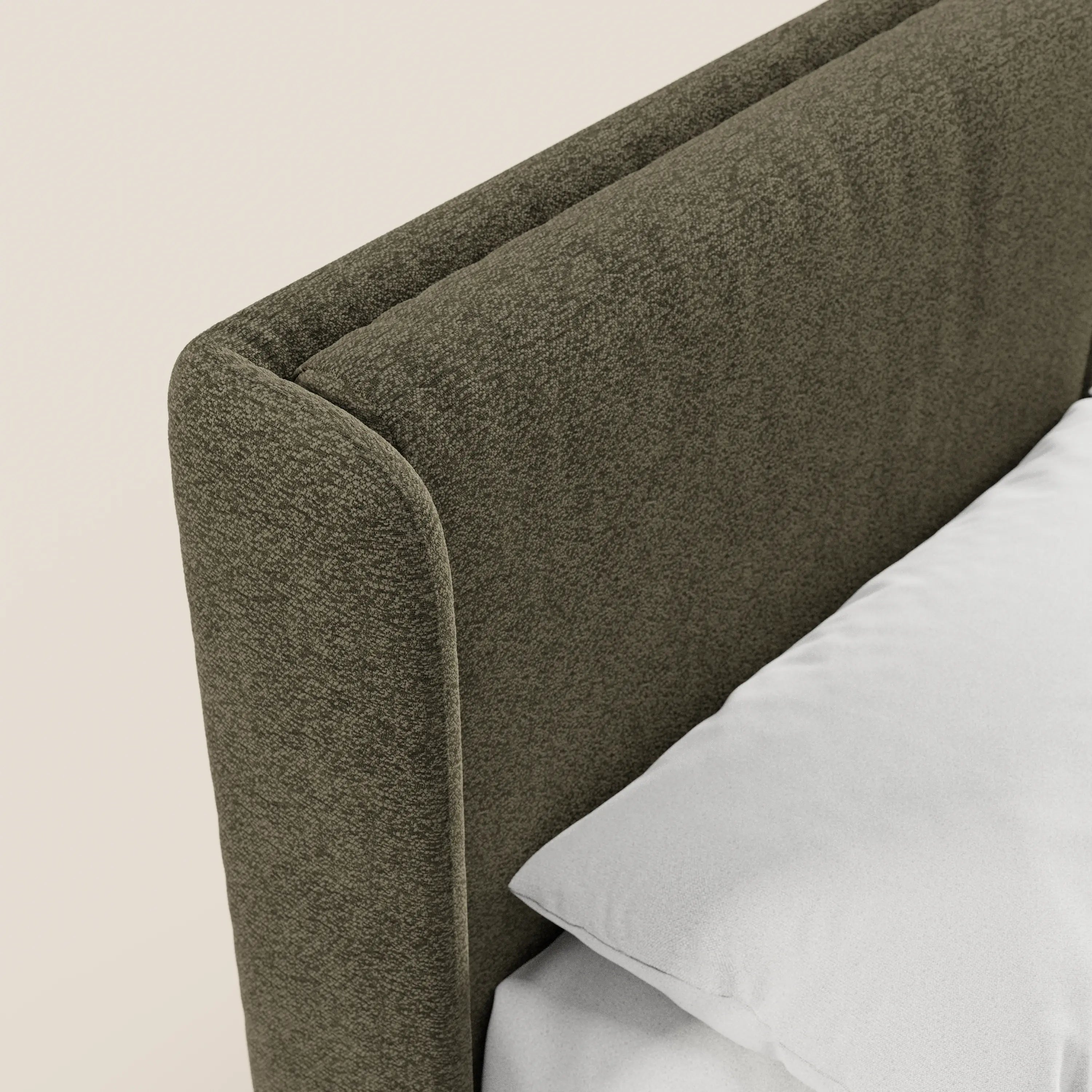 Primo piano del letto di design VALKIRIA di Letti.store, caratterizzato da una testiera imbottita in verde oliva certificata Oeko-Tex® con bordi arrotondati e 2 cuscini imbottiti. In un angolo, su uno sfondo beige, si intravedono un cuscino bianco e un lenzuolo.