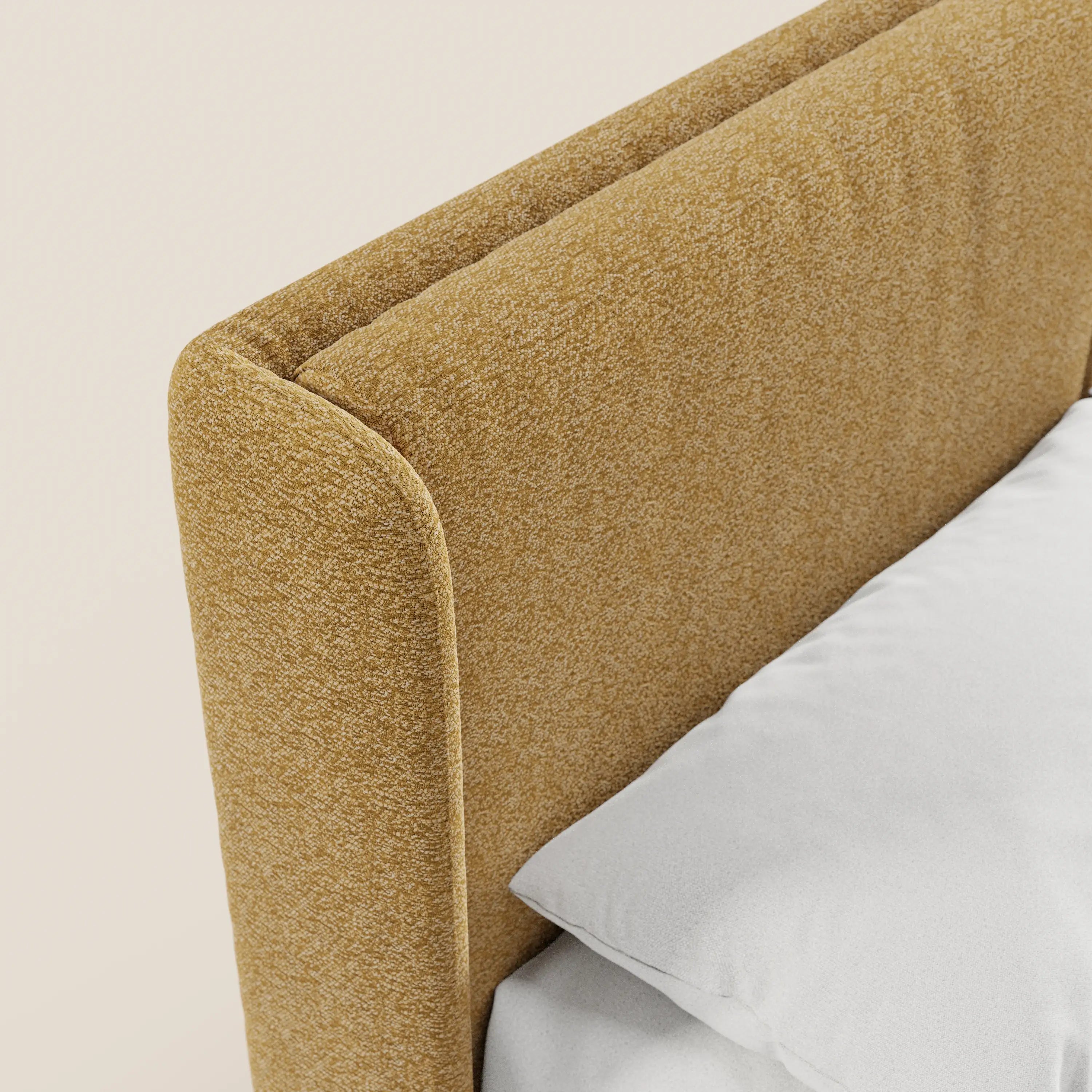 Questo primo piano del letto di design VALKIRIA di Letti.store mette in risalto la testiera in tessuto giallo senape certificato Oeko-Tex®, con bordi arrotondati e 2 cuscini imbottiti. Un cuscino e un lenzuolo bianchi creano un contrasto, accentuando lo stile contemporaneo del letto e la sua base contenitiva.