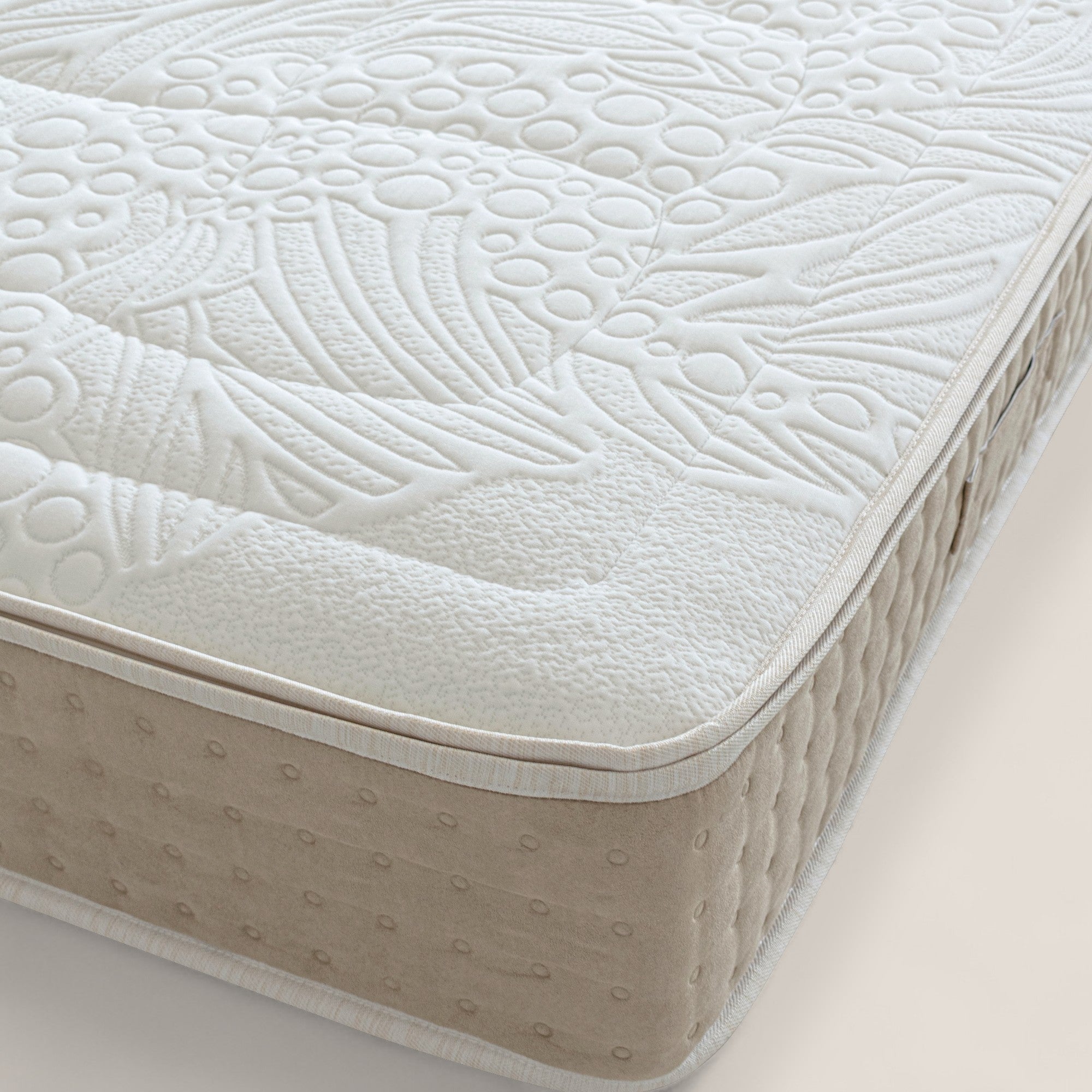 Primo piano di un materasso VELTHA di Divani.Store, che mostra un piano bianco con dettagliati motivi di foglie e cerchi in rilievo e un lato beige a pois. È dotato di insacchettato molleggiato e lattice naturale con supporto a 7 zone per il massimo comfort.