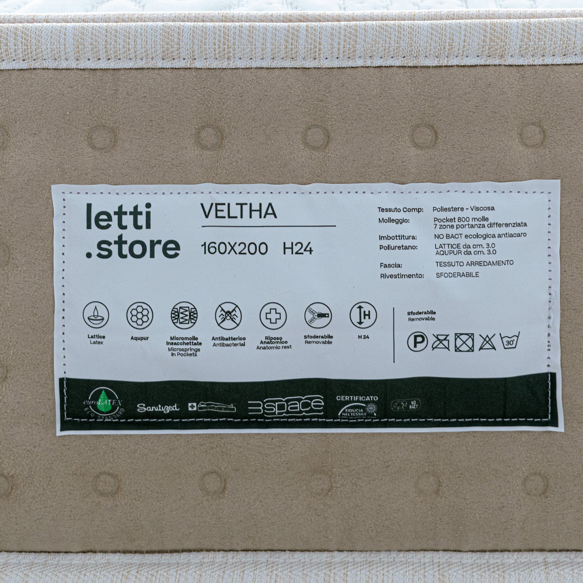 Un primo piano di un'etichetta "Divani.Store" VELTHA - Materasso Bio-Adattivo mostra la misura 160x200 H24, le molle insacchettate, il lattice naturale a 7 zone di adattamento, le informazioni sul tessuto, le istruzioni per la cura e le icone per il rivestimento antibatterico, anallergico e lavabile.