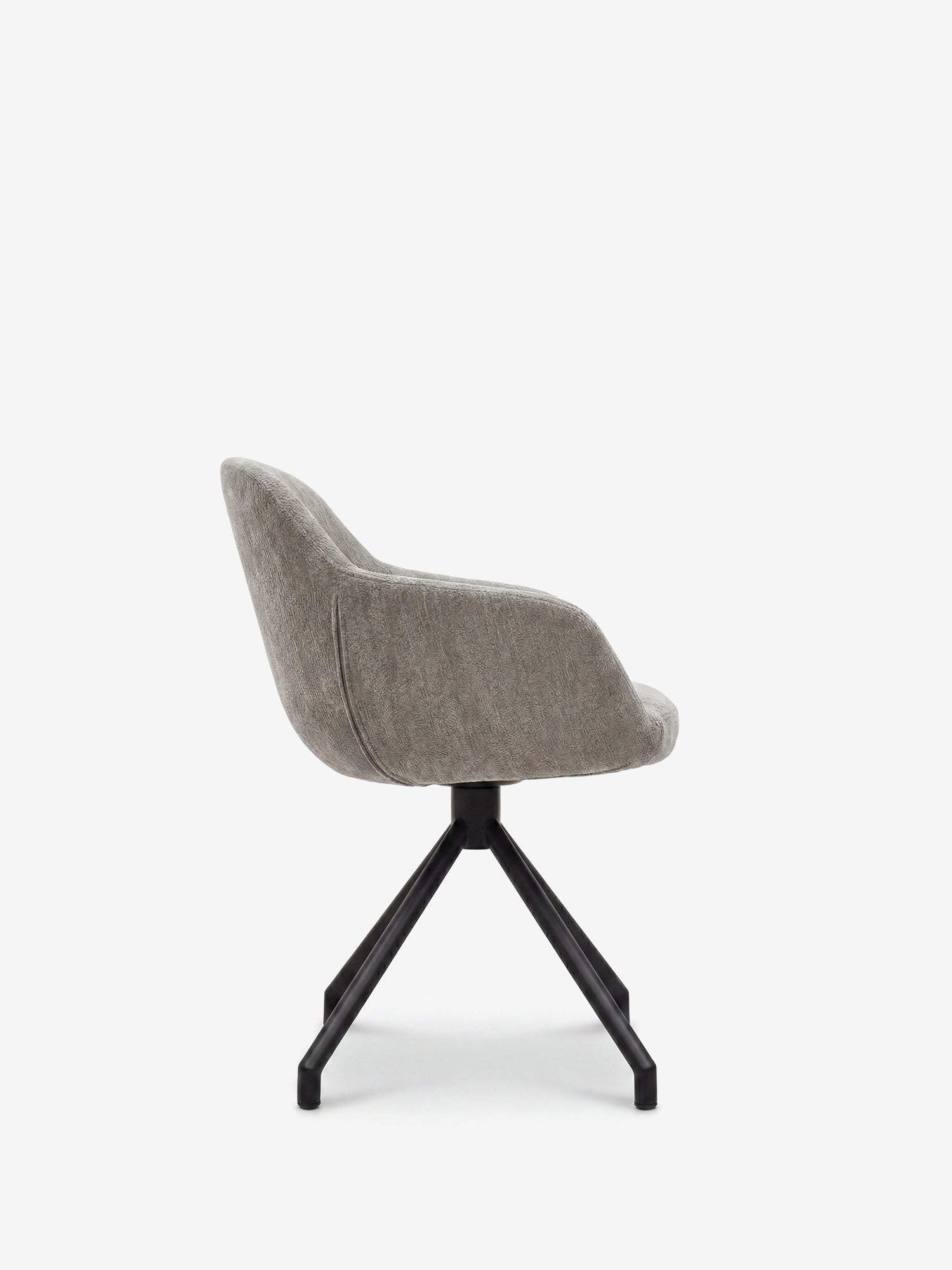 La sedia imbottita Vico di Divani.Store, realizzata in morbido tessuto grigio soft-touch certificato OEKO-TEX®, presenta uno schienale e una seduta curvi, con eleganti gambe in metallo nero che formano una base a stella a quattro punte; nella foto è raffigurata di profilo su uno sfondo bianco a tinta unita.