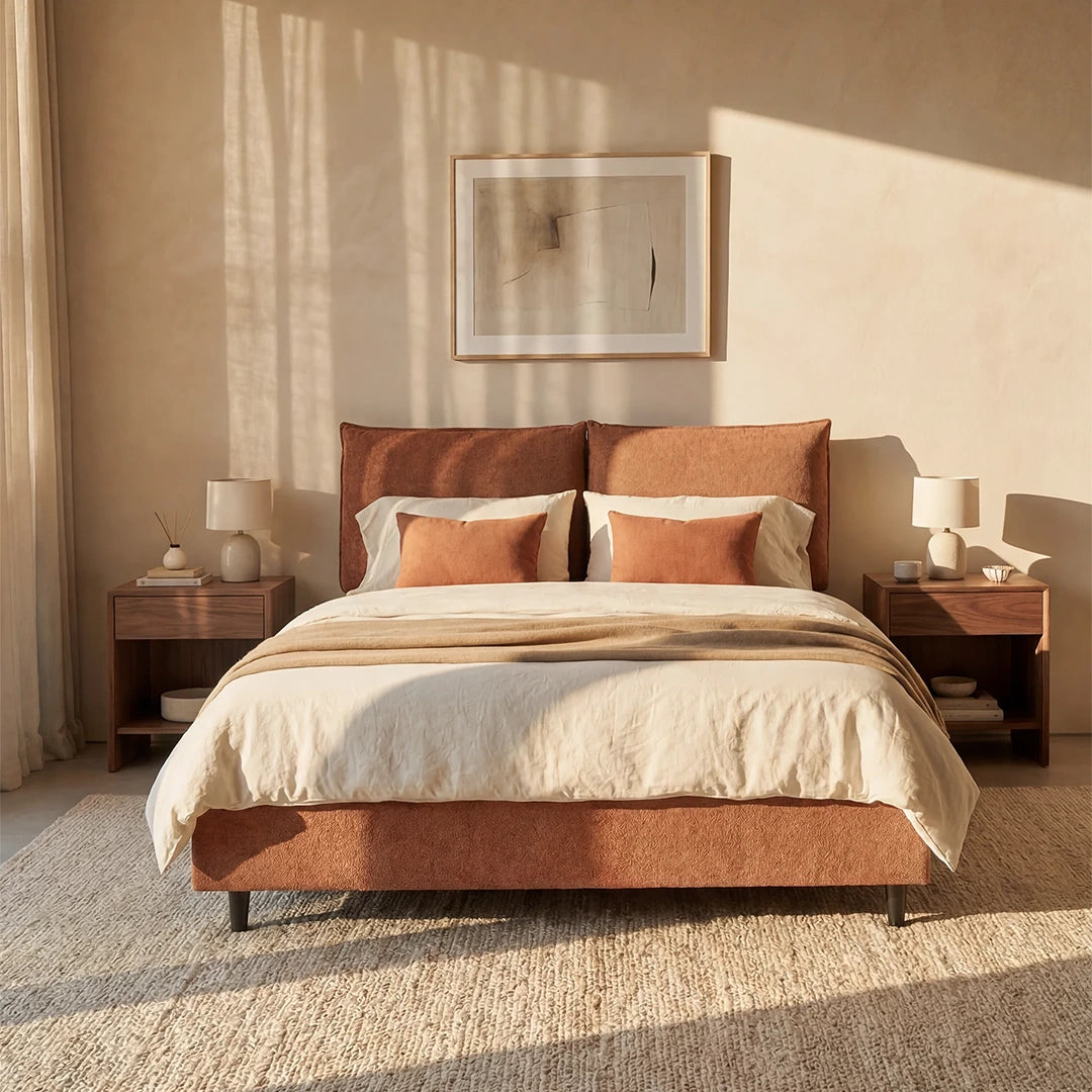 Una camera da letto luminosa e minimalista mette in risalto il letto imbottito ZAYRON di Letti.store, dotato di vano contenitore e morbidi cuscini regolabili in tessuto certificato Oeko-Tex®, abbinato a biancheria da letto beige, due comodini in legno, lampade bianche, opere d’arte astratte e un tappeto dalla trama ricca.