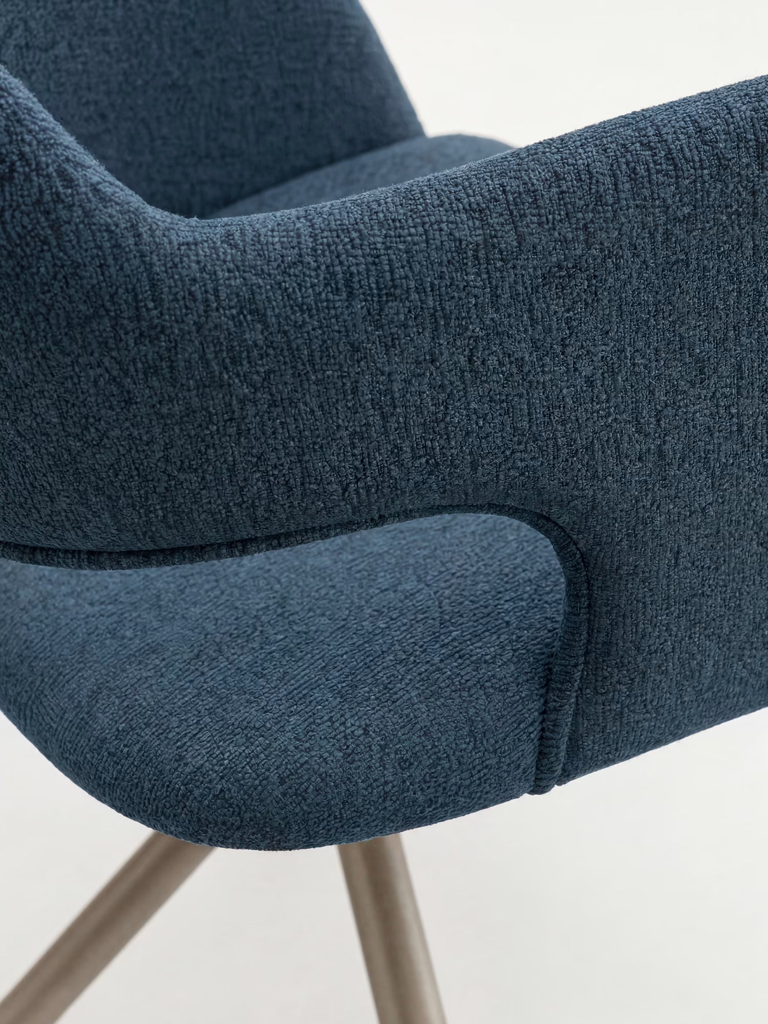 Primo piano della sedia di design Zefira Sedia imbottita con braccioli di Divani.Store, che ne mette in risalto il tessuto effetto cotone blu scuro, i braccioli ricurvi e la base in metallo con finitura champagne su uno sfondo chiaro e uniforme.