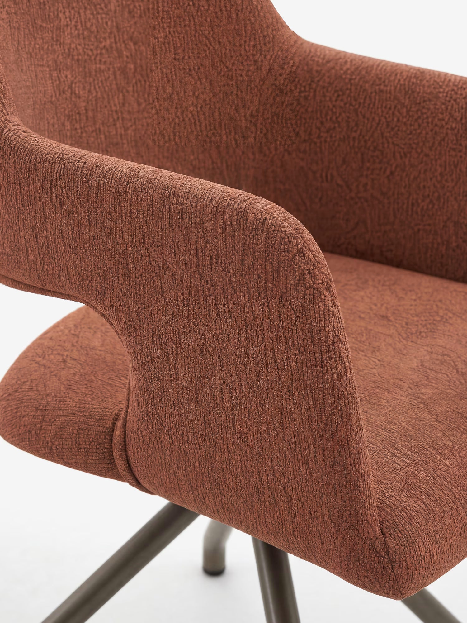 Primo piano della poltrona imbottita di design Zefira di Divani.Store, caratterizzata da un tessuto color ruggine dall’effetto cotone, braccioli ricurvi e una base in metallo color champagne opaco. L’immagine mette in risalto la delicata trama della seduta e una parte della gamba.