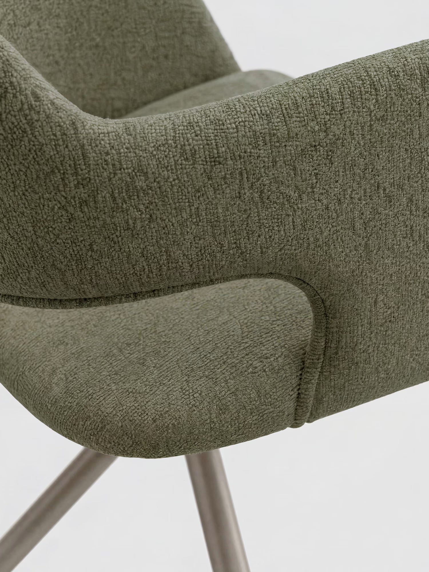 Primo piano della poltrona di design Zefira con braccioli di Divani.Store, realizzata in tessuto effetto cotone color verde oliva e con base in metallo color champagne. Silhouette moderna con braccioli dalle linee morbidamente curve; lo sfondo è a tinta unita e di colore chiaro.