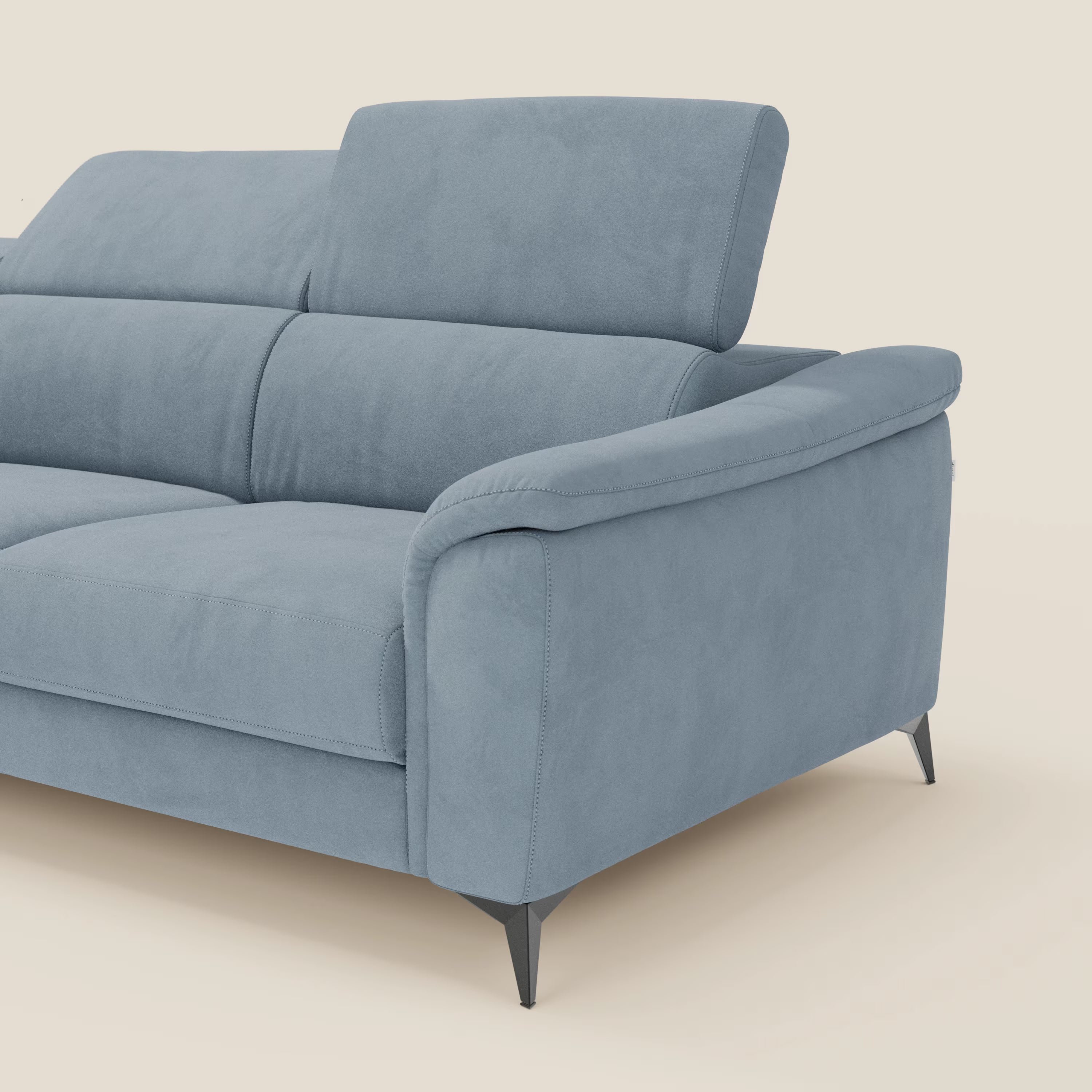 L'Arcos Divano con penisola di Divani.Store, in microfibra impermeabile T11 carta da zucchero, ha piedini alti neri e poggiatesta reclinabili. Solo la metà destra è visibile, su sfondo crema chiaro.