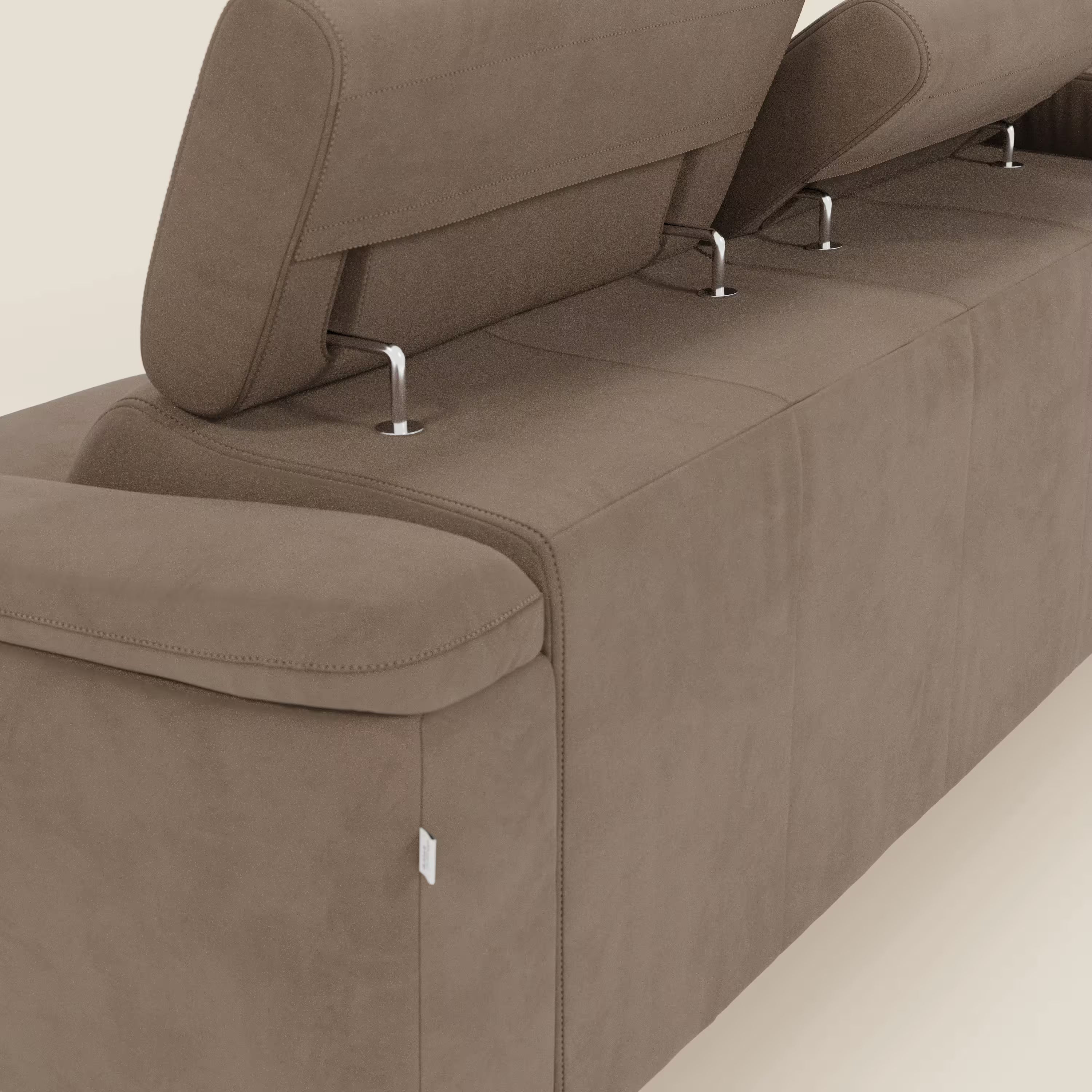 Un primo piano dell'Arcos Divano con penisola di Divani.Store in microfibra impermeabile T11 marrone mostra i poggiatesta regolabili, gli alti piedini in metallo, le raffinate cuciture e la targhetta bianca sul bracciolo: eleganza e funzionalità.