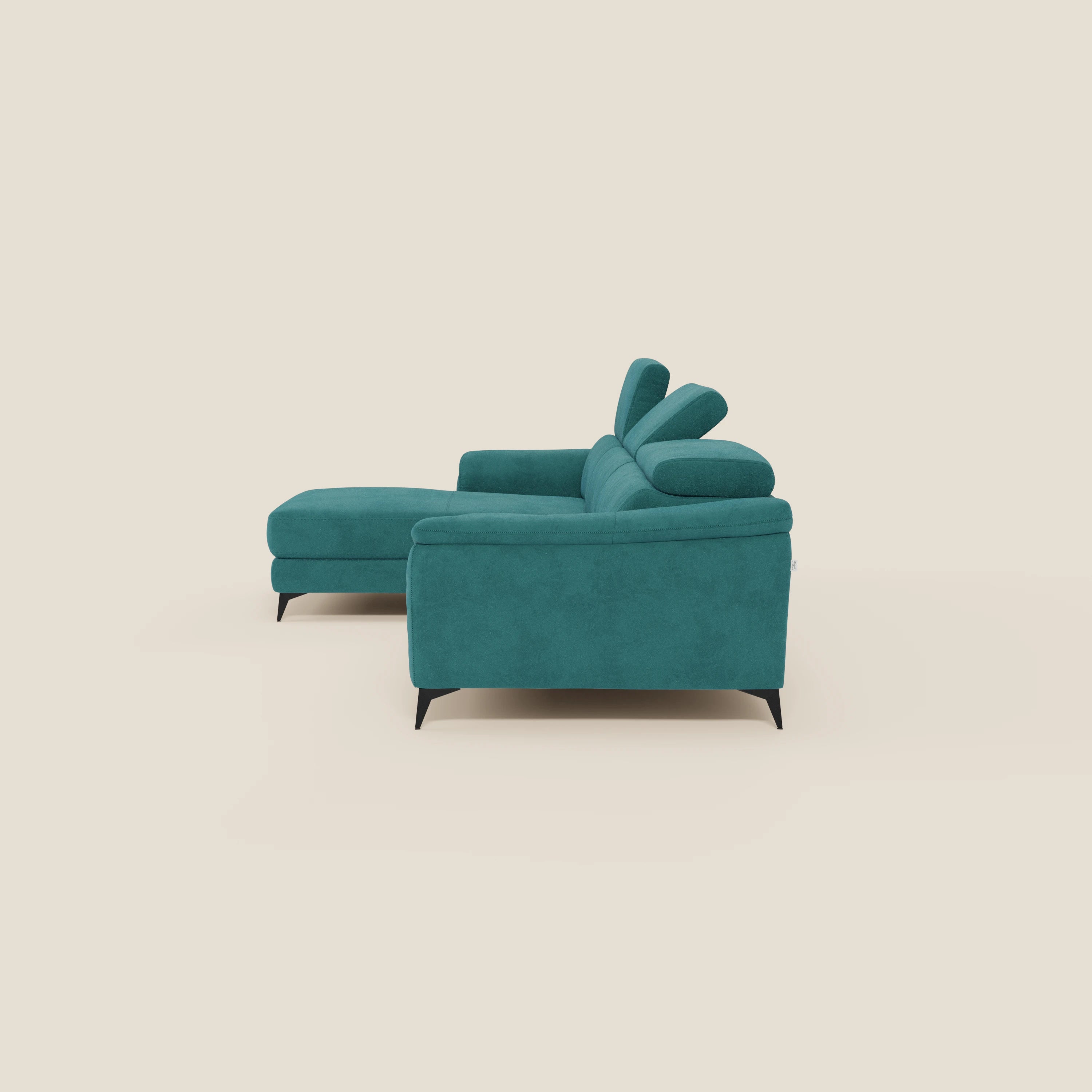 L'Arcos Divano con penisola di Divani.Store, in microfibra impermeabile T11 petrolio con gambe alte nere e poggiatesta reclinabili, è presentato di lato su uno sfondo beige chiaro.