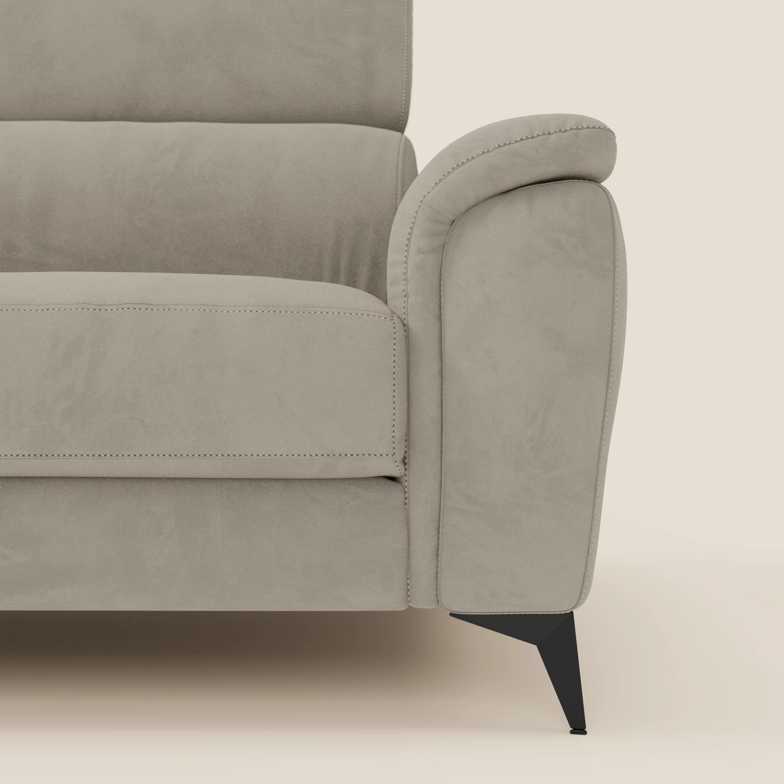 Primo piano di Arcos Divano 3 posti di Divani.Store in microfibra impermeabile T11 tortora, che mostra il bracciolo e il cuscino di seduta arrotondati e cuciti. Il divano è caratterizzato da sottili gambe in metallo nero e da un fondo bianco sporco.