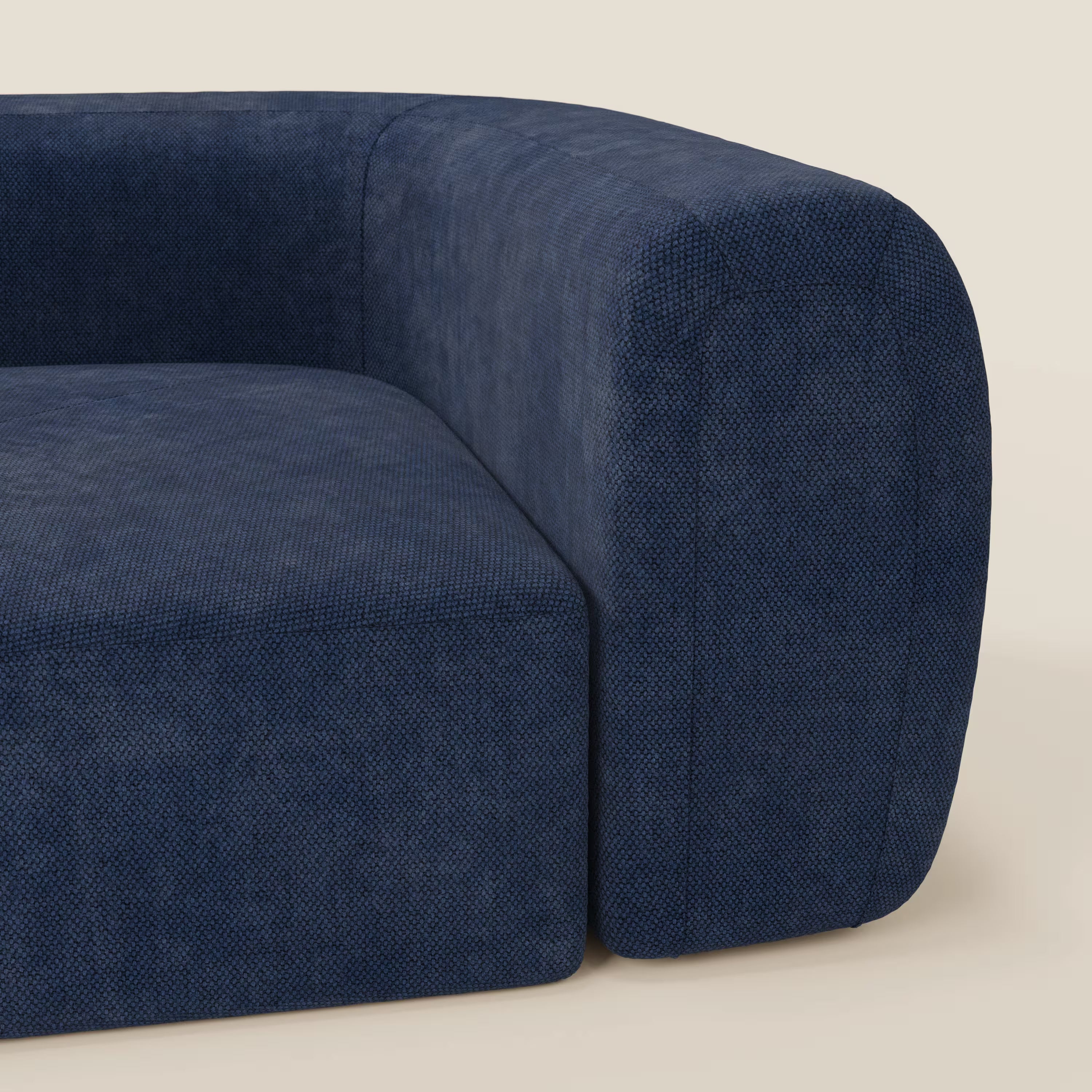Un primo piano del BonBon Modulo angolare - Divano componibile GF edition blu navy di Divani.Store mostra il rivestimento blu scuro, il bracciolo e la seduta spessi e arrotondati, su uno sfondo beige chiaro, che mette in risalto il design minimalista e curvilineo.